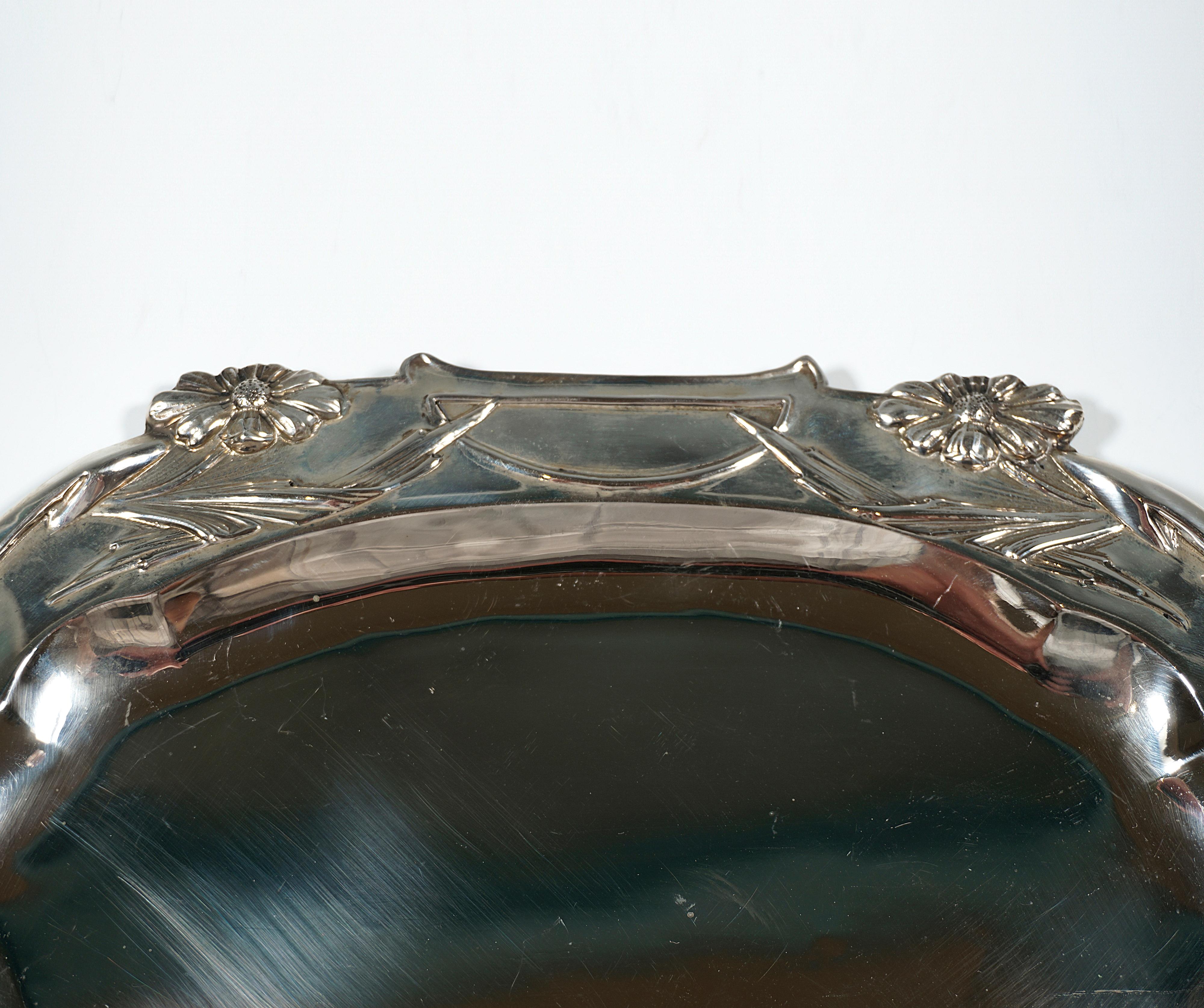 Petit plateau en argent avec miroir de forme ovale de base, large bord décoré d'un relief floral et poignées en forme de rubans prolongeant l'ovale en une navette.

Des poinçons :
Tête de Diane - Poinçon officiel autrichien 1872-1922 pour 800 pièces