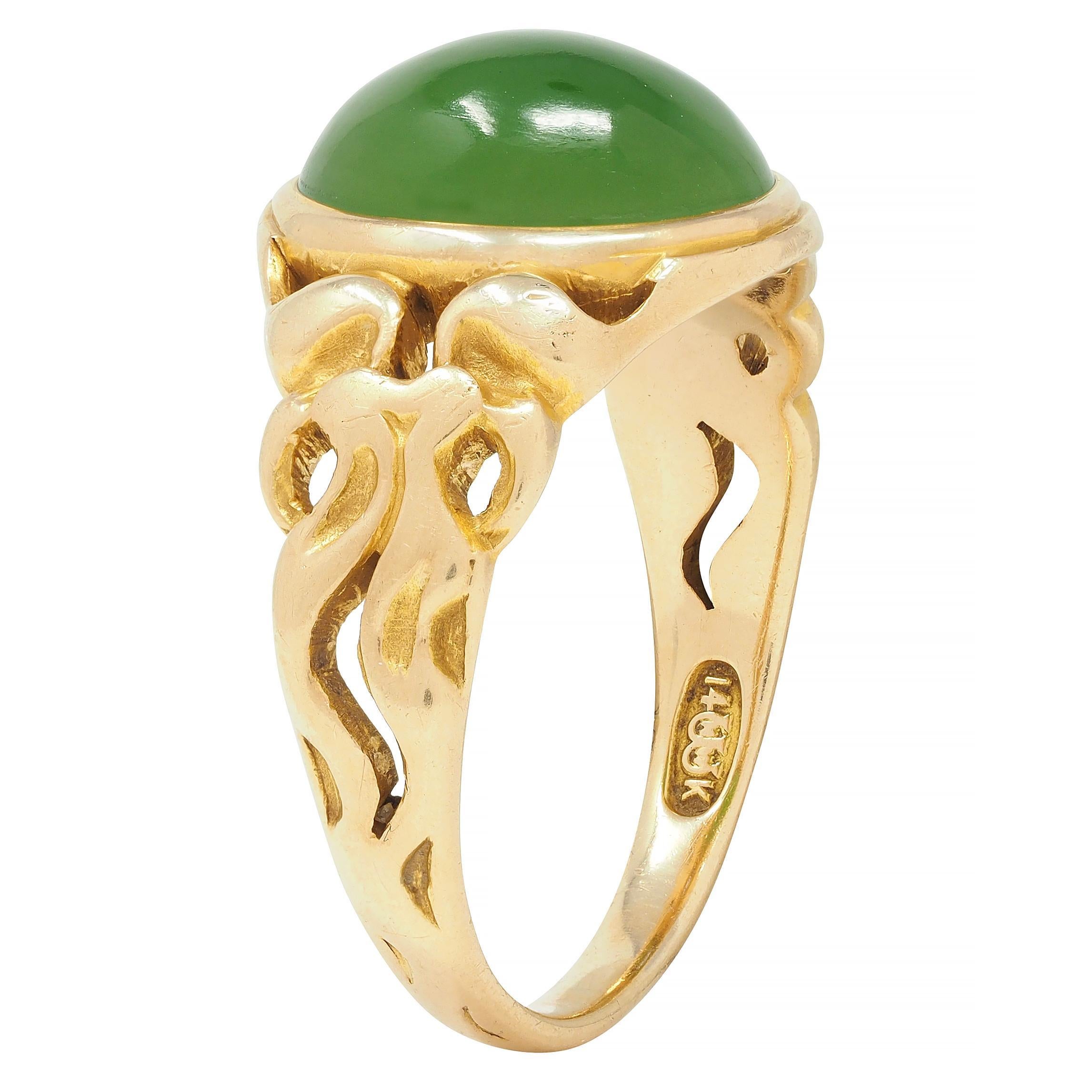 Centering a oval-shaped nephrite jade cabochon measuring 9.1 x 11.9 mm - opaque green with medium saturation 
Bezel set in a yellow gold surround
Accented by pierced stylized bow motif shoulders with pattern extending to base 
Stamped for 14 karat