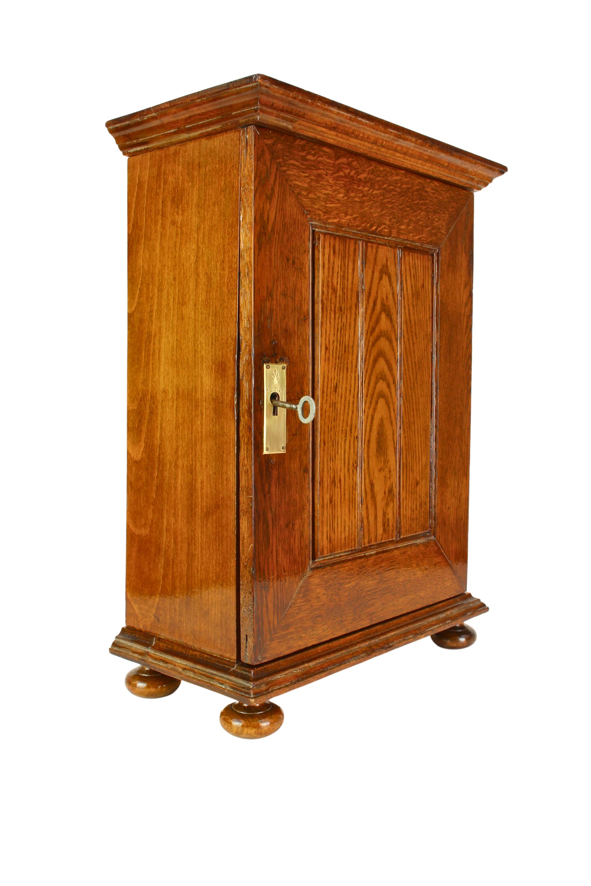 Charming Art Nouveau oak wall cabinet from Germany around 1900.
This small apothecary style cabinet features a finely crafted solid oak corpus with a warm, natural patina and a framed, paneled door with brass escutcheon and working key. The interior