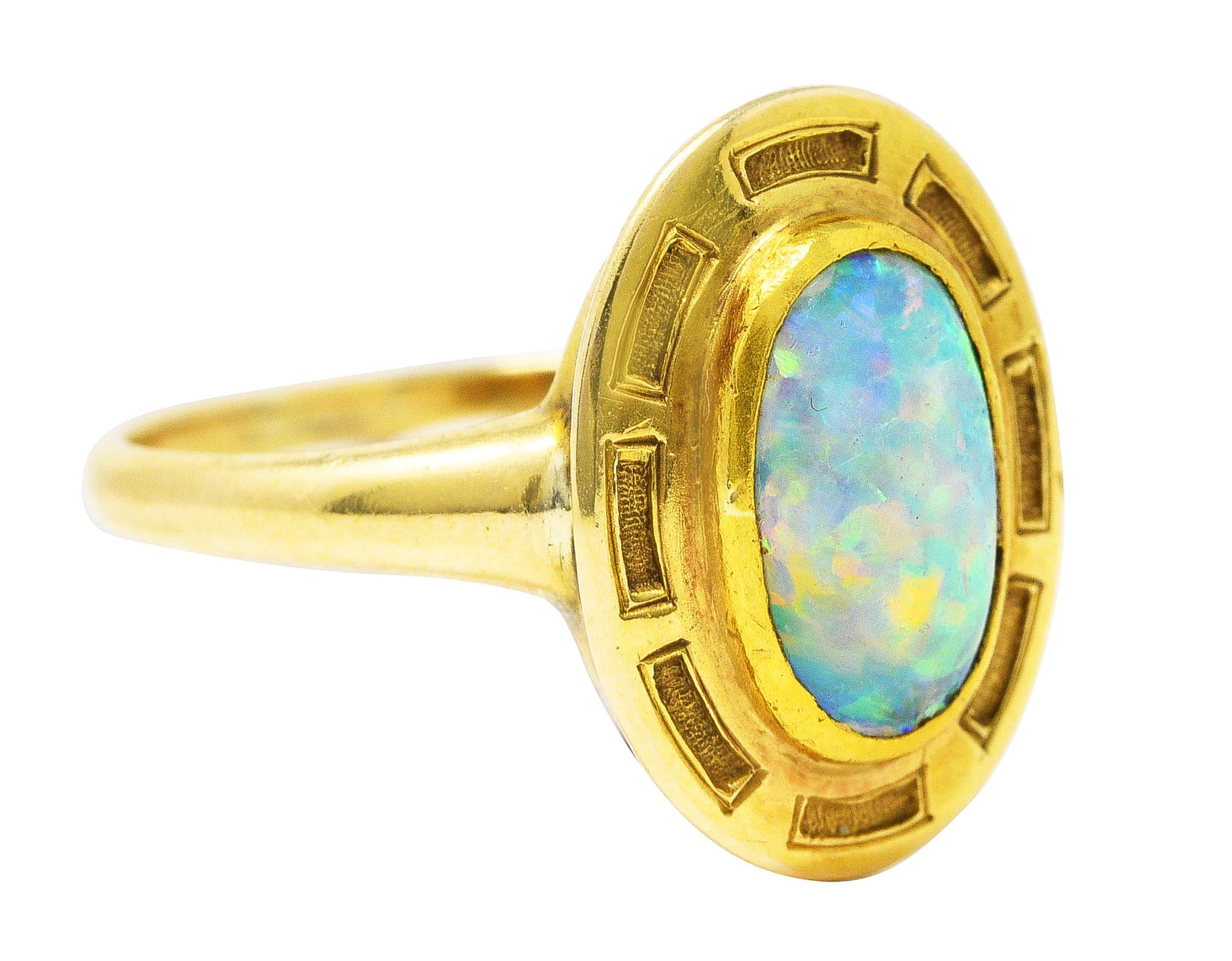 Ring centers a bezel set 6.0 x 9.1 mm oval opal cabochon. White in body color with excellent spectral play-of-color. With gold surround accented by textured rectangular recesses. Tested as 14 karat gold. Circa: 1900's. Ring size: 5 3/4 and sizable.