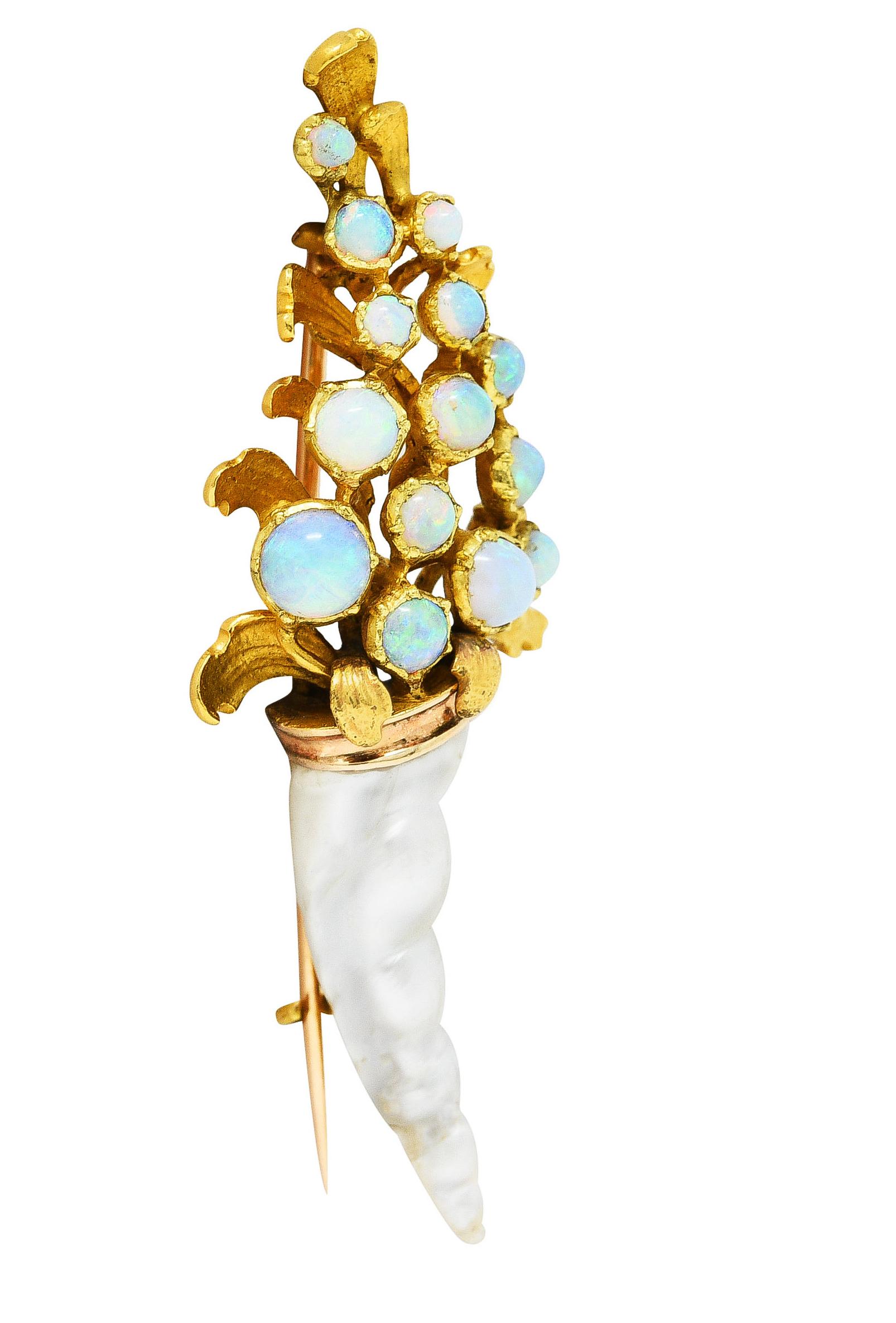 Designed as a stylized bouquet with opal cabochon flowers measuring 2.0 to 4.5 mm round. Translucent white in body color with spectral play-of-color.Prong set among rendered curling gold foliage. Emerging from a baroque pearl basket - carved with