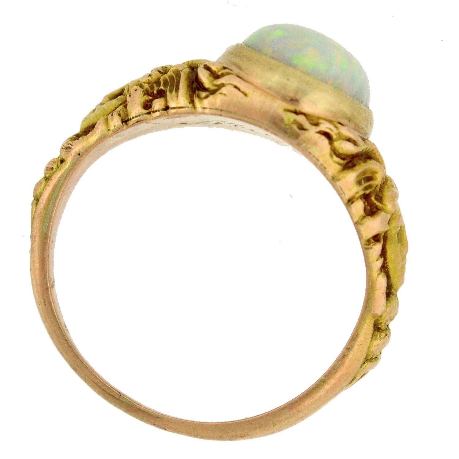 A stunning opal ring from the Art Nouveau (ca1900) era! This piece is crafted in 14kt yellow gold, and adorns a stunning opal cabochon at the center of a gorgeous repousse design. The bezel-set stone exhibits a mesmerizing array of shimmery
