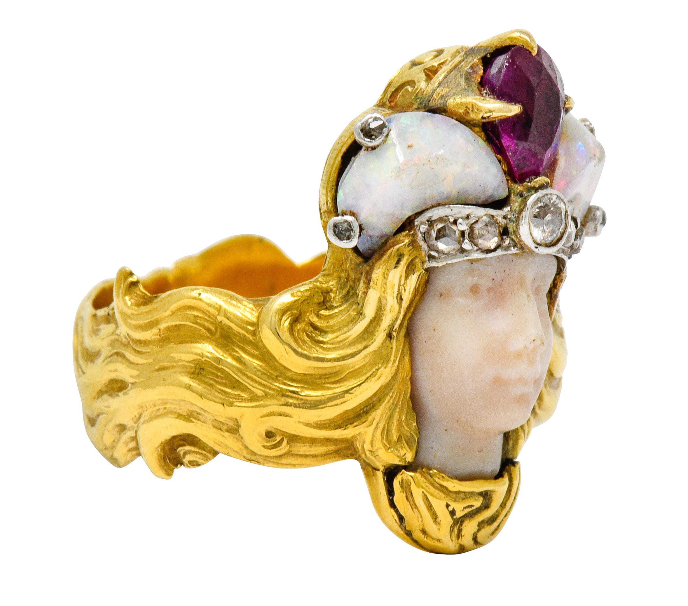 Designed as an empress carved from beige hardstone topped by a gemmed crown

Featuring a pear cut ruby, two tumbled opal, and accented by rose cut and old European cut diamonds

Hairline crack in one opal and chip at nose; consistent with age

Band