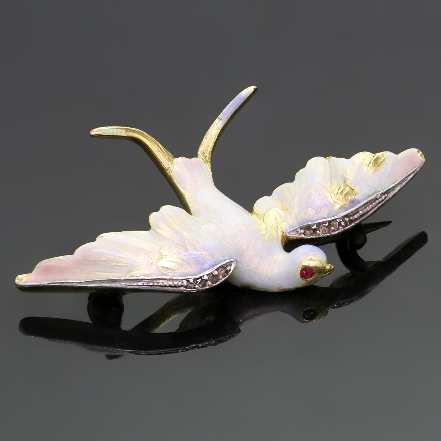 This rare Art Nouveau brooch is crafted in 14k yellow gold in the shape of opalescent golden blue enamel bird accented with ruby eyes and single cut diamonds set in platinum wings. Due to age of this antique, there is enamel missing in a few spots.