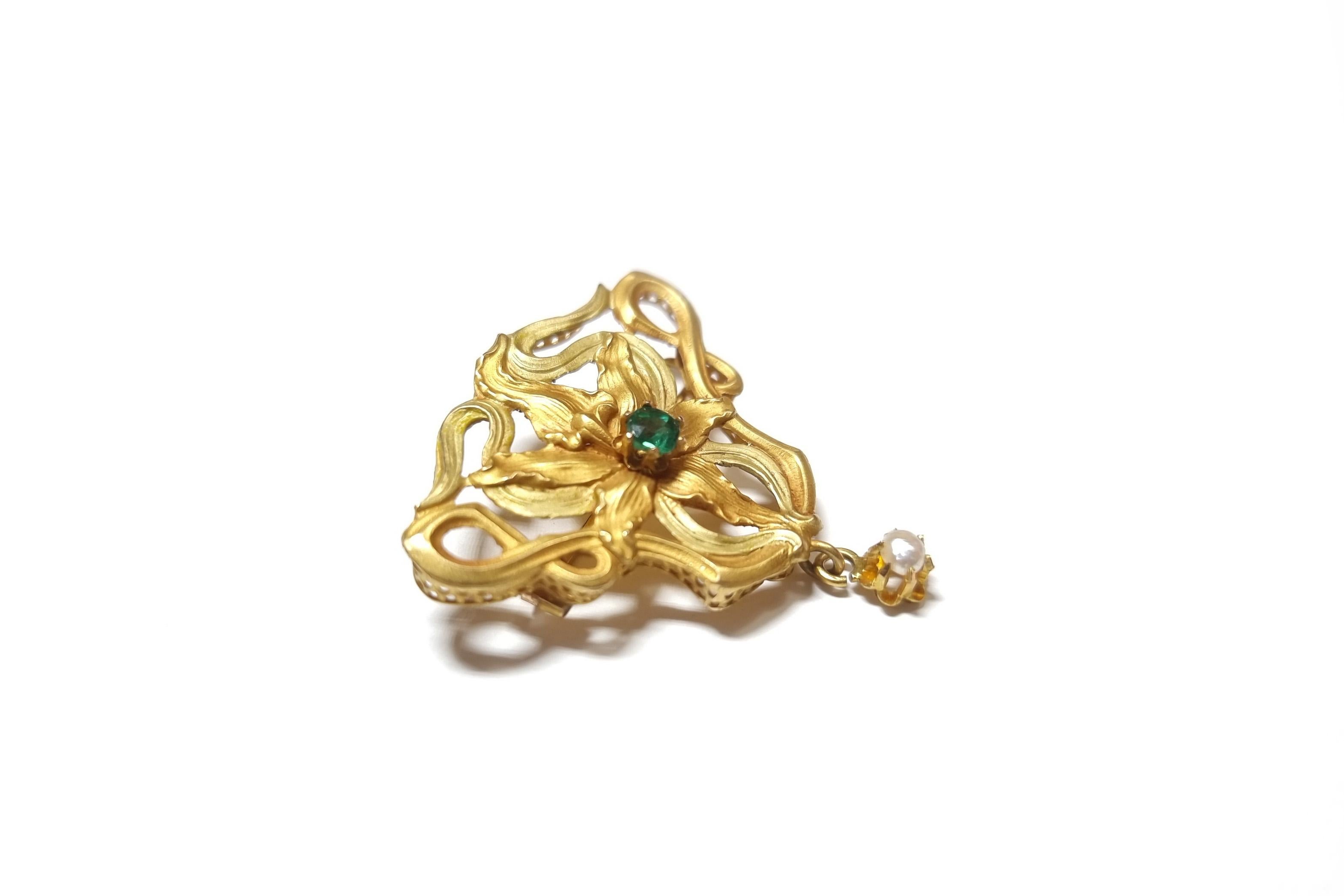 Art Nouveau orchid brooch in 18 karats matte gold, yellow and green colors, with a triangular shape and decorated with an orchid flower in full bloom centered with a green stone (garnet /glass doublet), surrounded by 