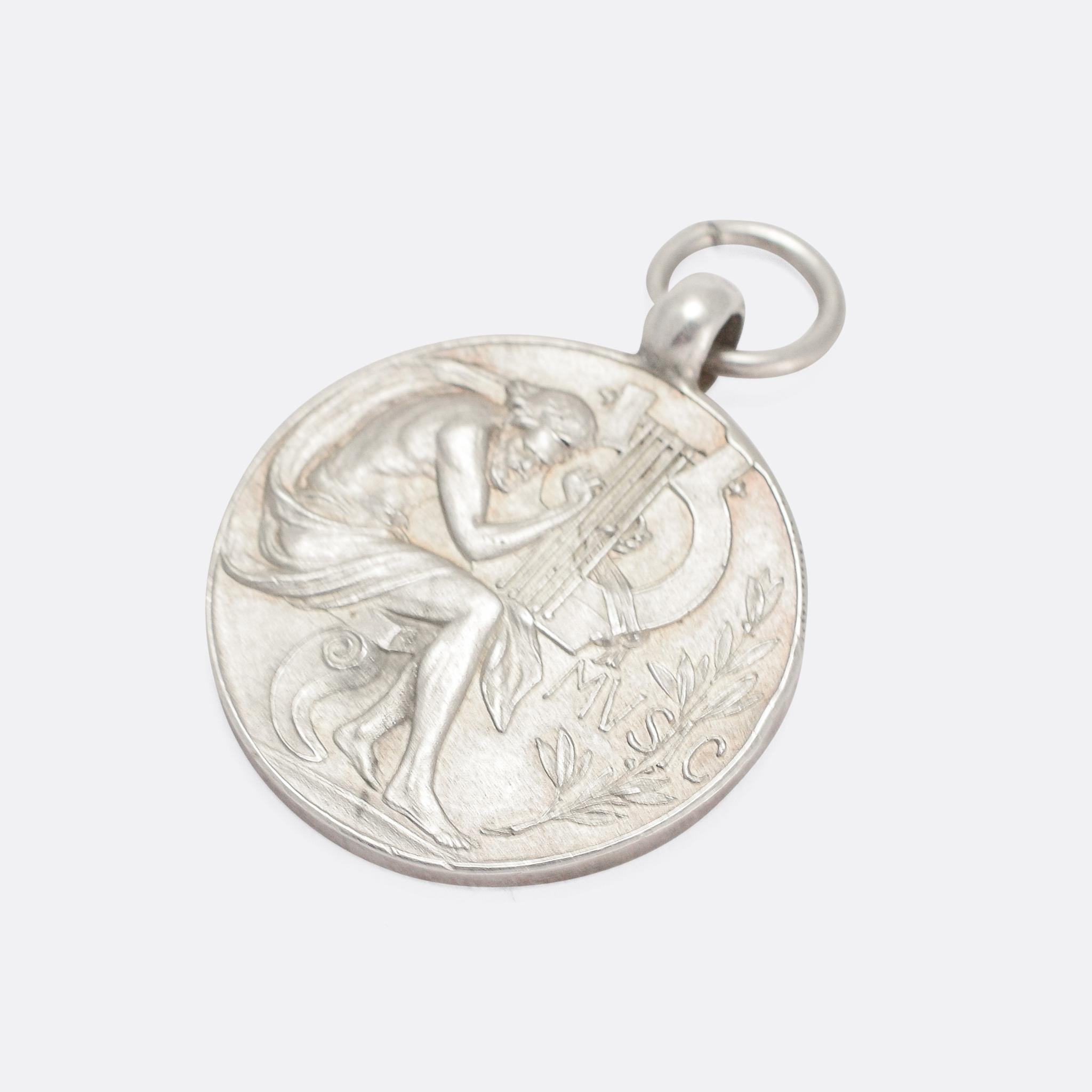 A fine antique medallion pendant featuring Orpheus playing the lyre, next to the word MUSIC. It's modelled in sterling silver, and dates from the early 20th Century. 

MEASUREMENTS 
3.2 x 2.6cm (not including jump ring)

WEIGHT 
8.9g

MARKS 
English