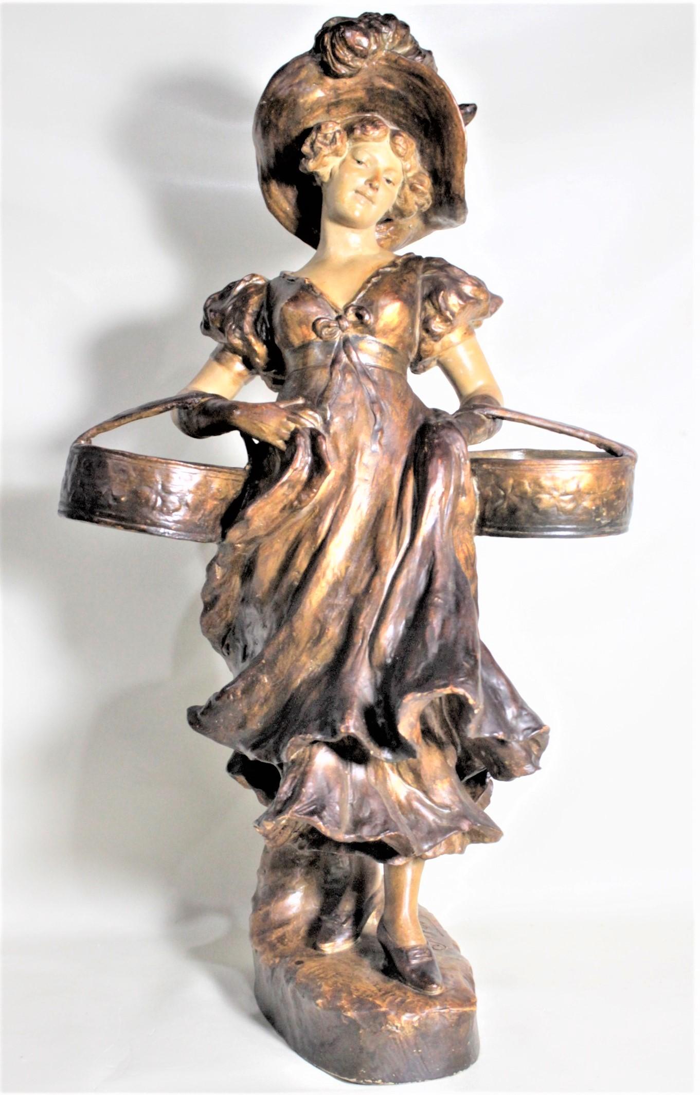 This glazed earthenware sculpture was done by the German sculptor, Otto Petri in the period Art Nouveau style. This sculpture is a very detailed depiction of a young woman with a flowing dress and hat, carrying two baskets, possibly to market. The