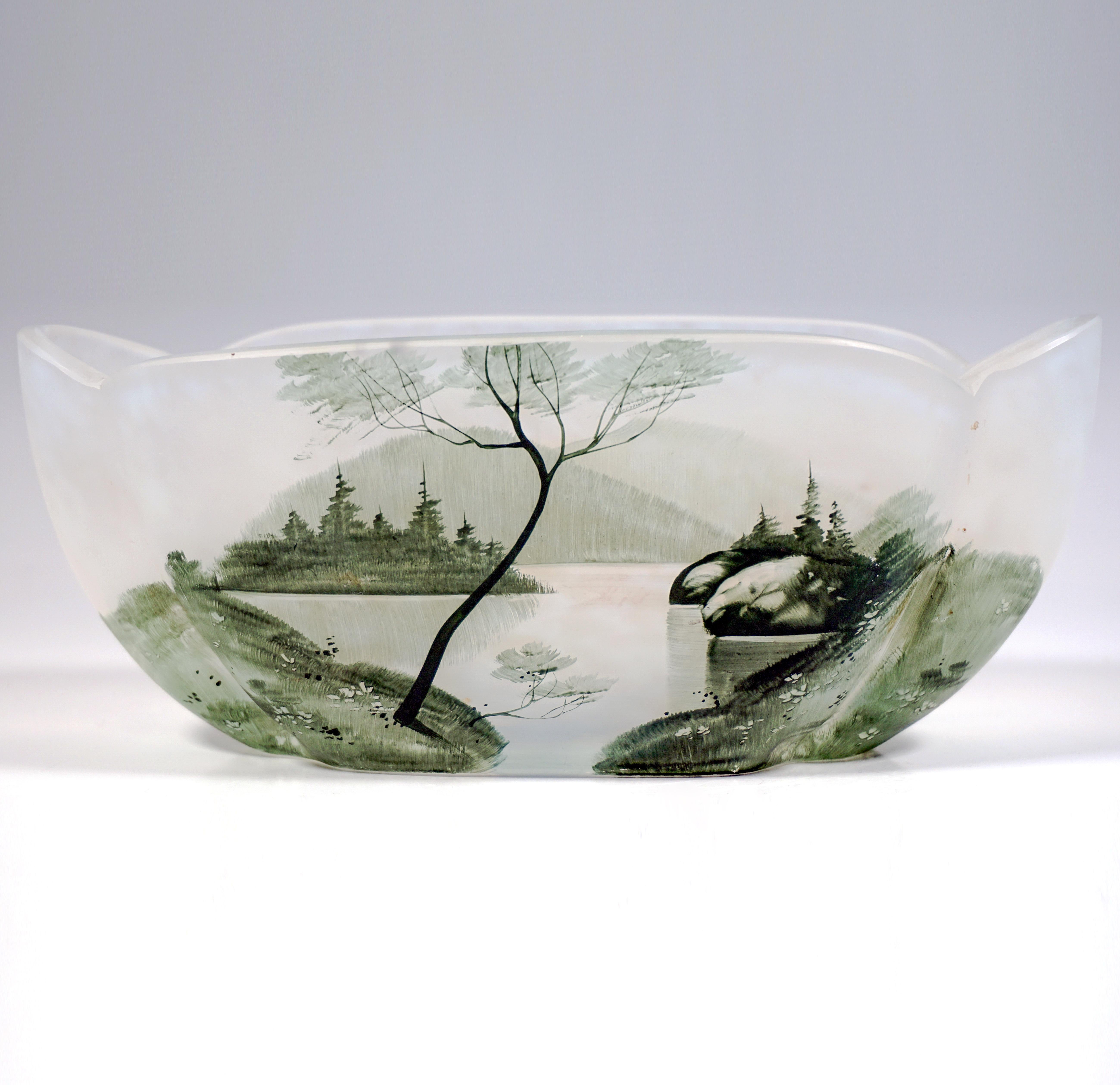 Delicato vetro artistico di Nancy del primo periodo dell'Art Nouveau francese:
Ciotola ovale a forma di quatrefoglio con pieghe e bordo curvo, vetro incolore con fusioni di polvere bianca a scaglie, lago e paesaggio collinare finemente dipinti in