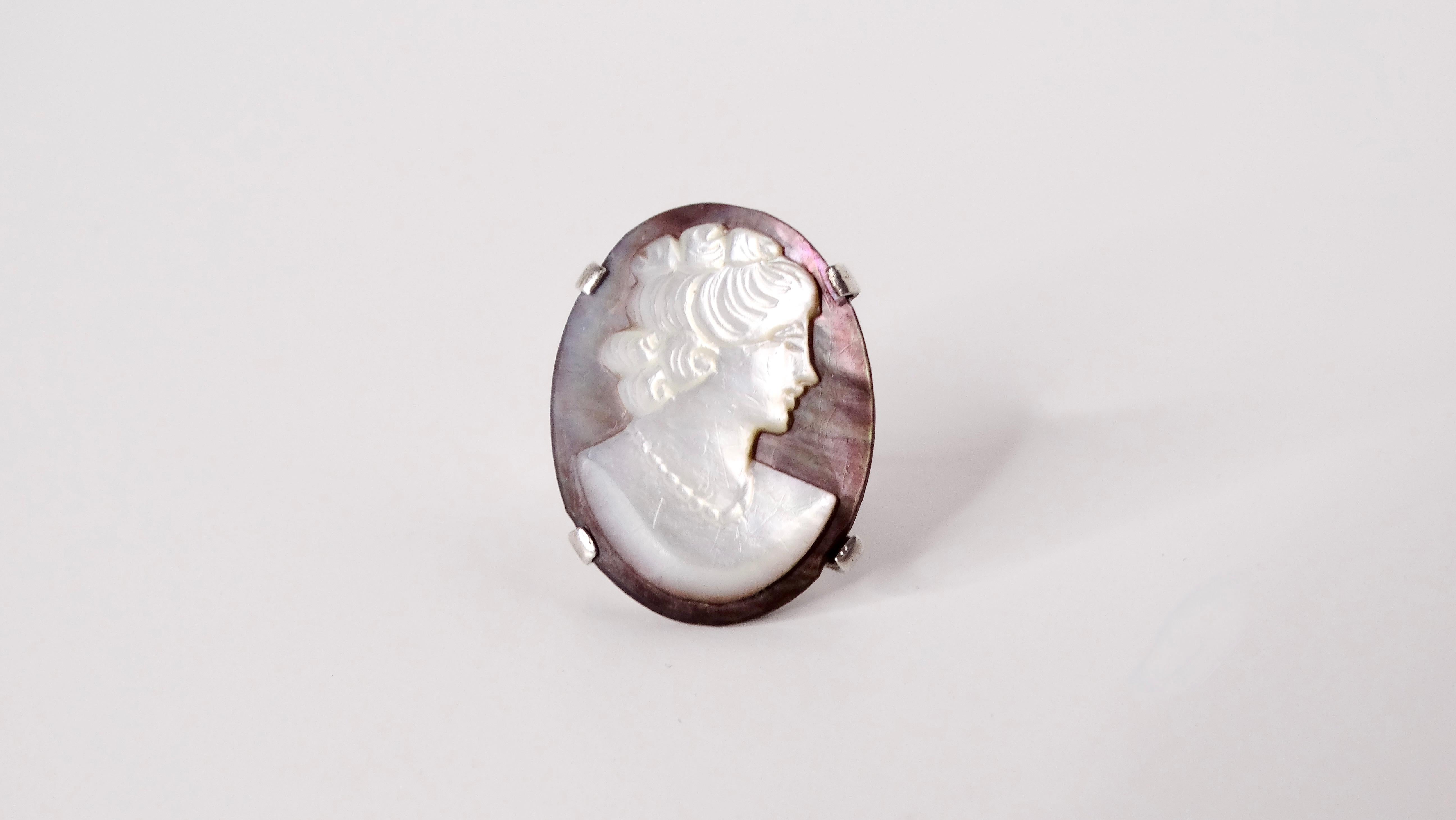 This exquisite Art Nouveau oval ring features a mesmerizing iridescent purple shell base and cameo silhouette of a woman, artfully set in lustrous sterling silver. The intricate design draws inspiration from the fluid lines and organic forms