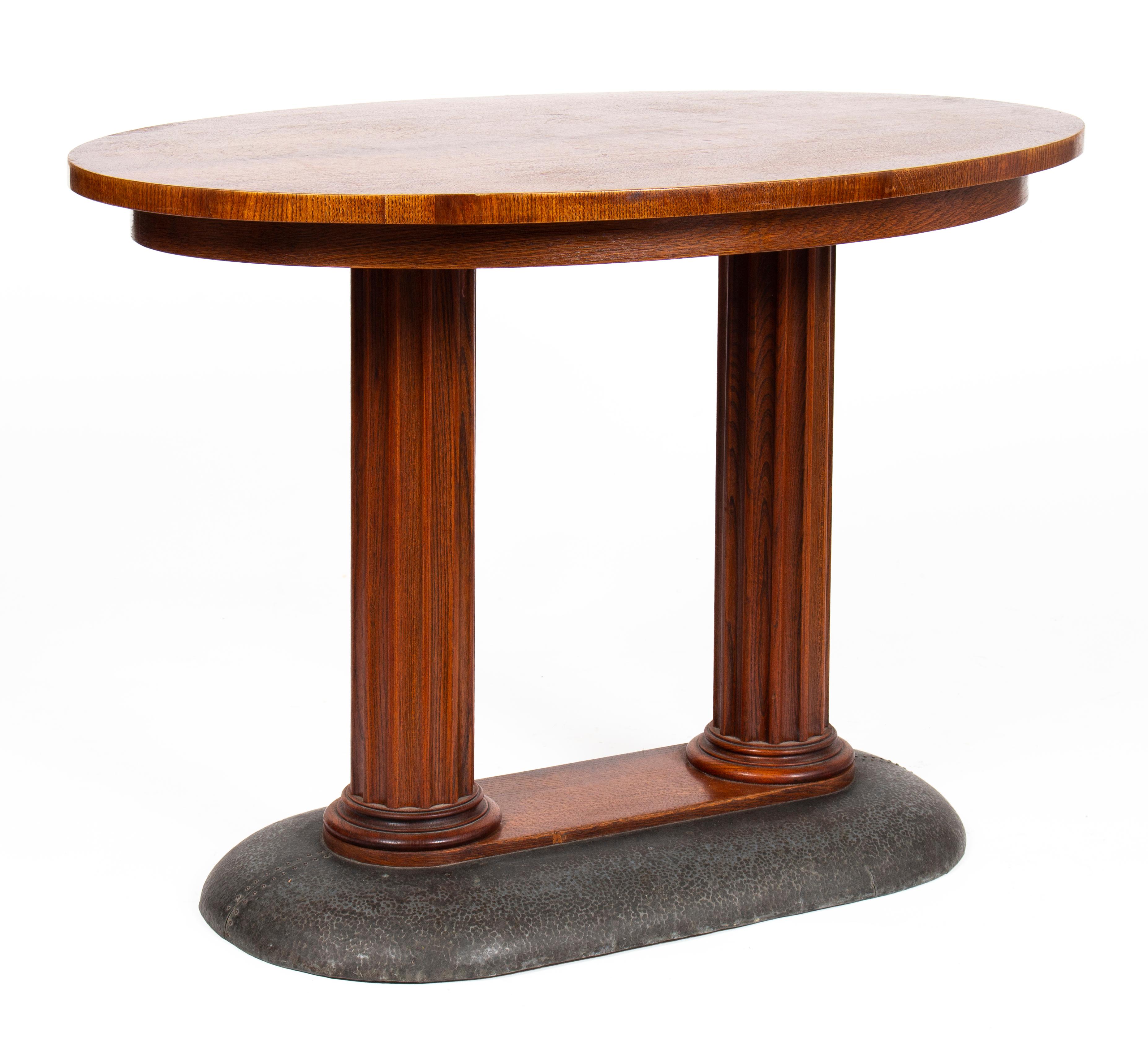 Secession center table, of elegant oval shape. Standing on two fluted columns, emerging from a solid bronze base.
The table top has a fine oak veneer surface, giving it a natural colour, complemented by the shimmer of the hammered bronze surface.
 