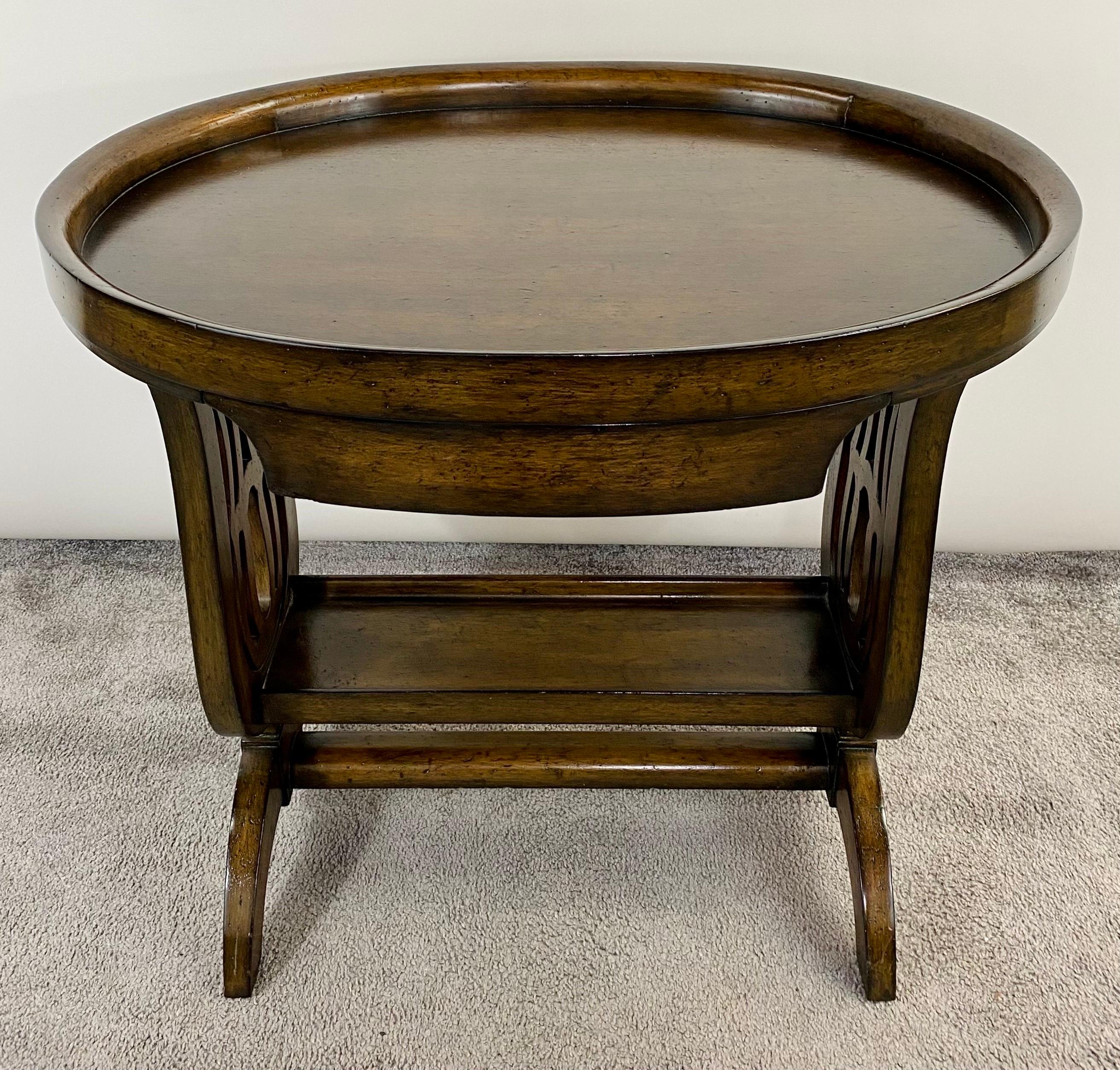 An exquisite oval walnut library or tray table featuring a sleek hidden drawer under the tray or table top. The two-tier table offers a small Bottom shelf. The side of this stunning piece are finely carved in beautiful curvy design adding class and