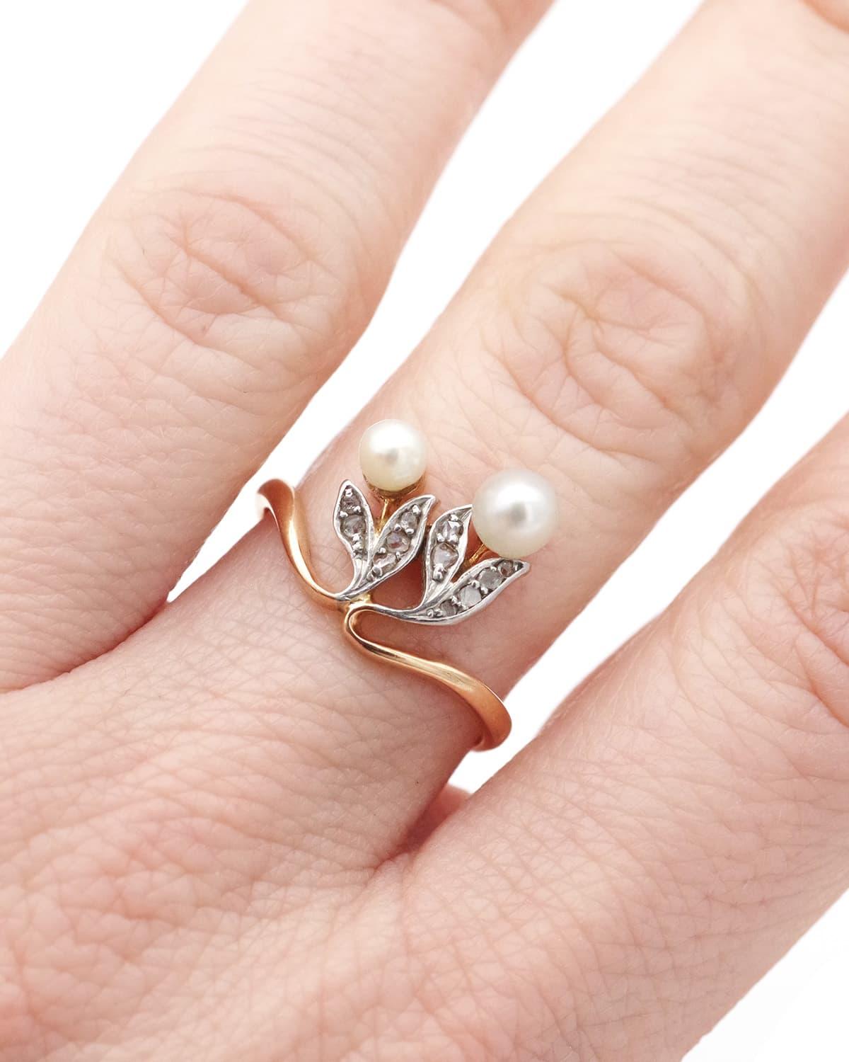 Anello di perle Art Nouveau in oro 18 carati e platino. L'anello presenta due fiori con diamanti taglio rosa incastonati, mentre i boccioli sono simboleggiati da due belle perle. Le foglie sono di platino. Questo anello presenta forme sinuose e