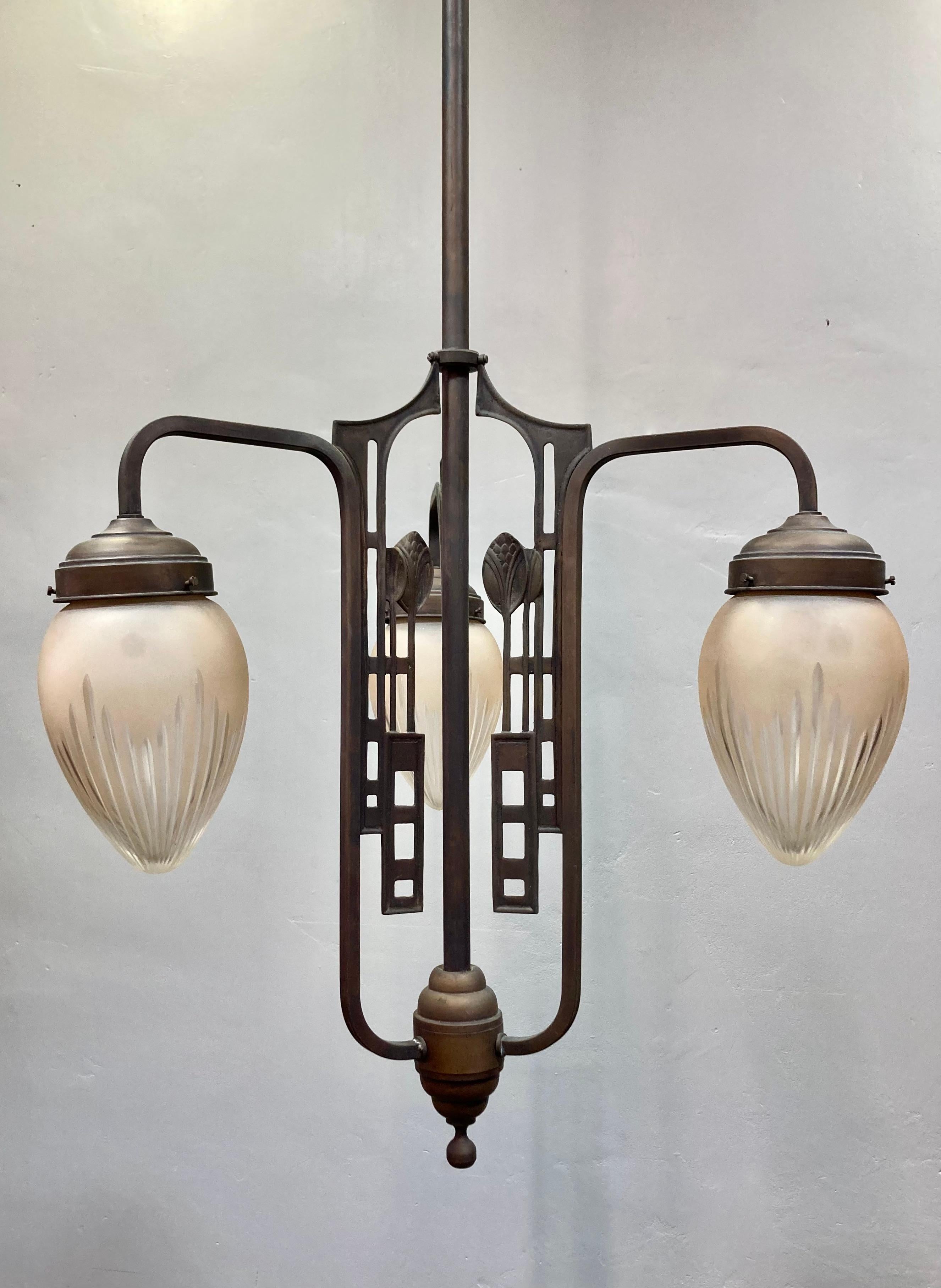 Art nouveau (1920's - 30's) pendent chandelier. Brass hardware and frosted glass bulb shades. Classic geometric patterning with foliage motifs. Holds 3 lightbulbs. 

19