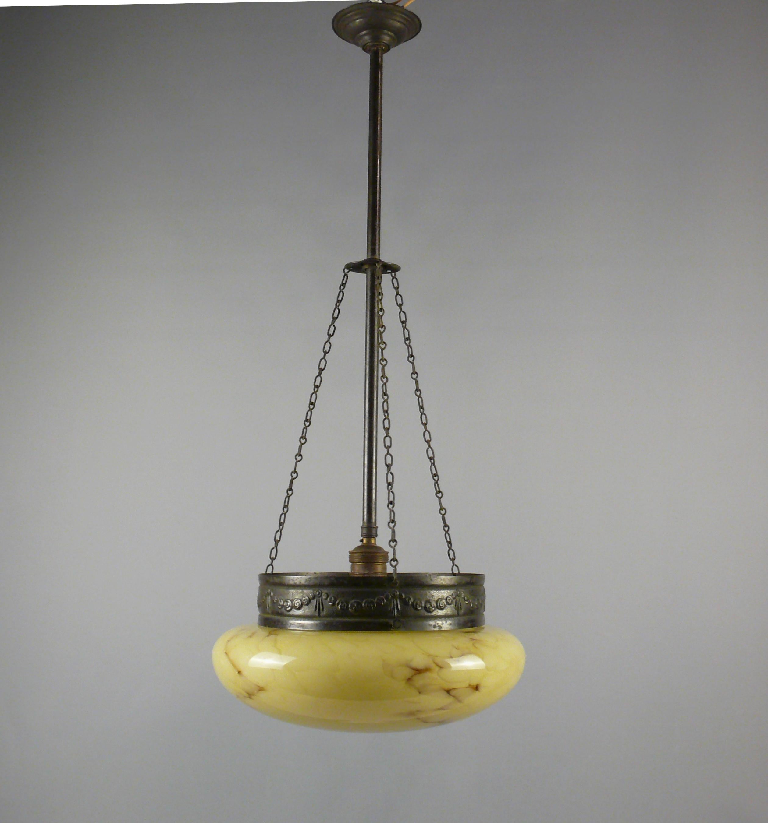 

Pendant lamp from the 1910s - 1930s with a marbled glass shade and in very good condition. The dark yellow glass shade has a beautiful shape and subtle marbling. The elaborate bronze suspension consists of a pendulum rod that holds the socket and