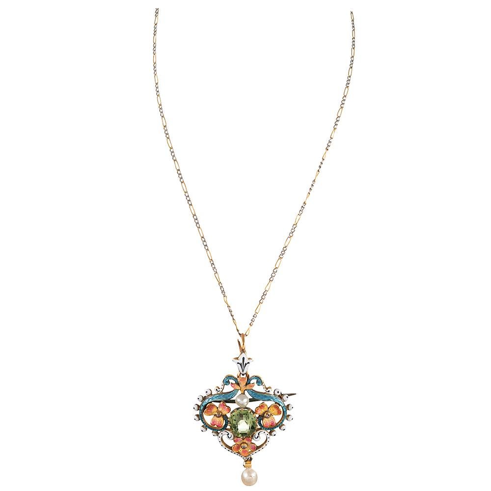 A beautifully styled 18 karat yellow gold pendant, created in the traditional art nouveau style with a peridot at its center. The major stone is framed by an elaborate backdrop of fanciful enamel with a frilled edge of speckled white complimenting