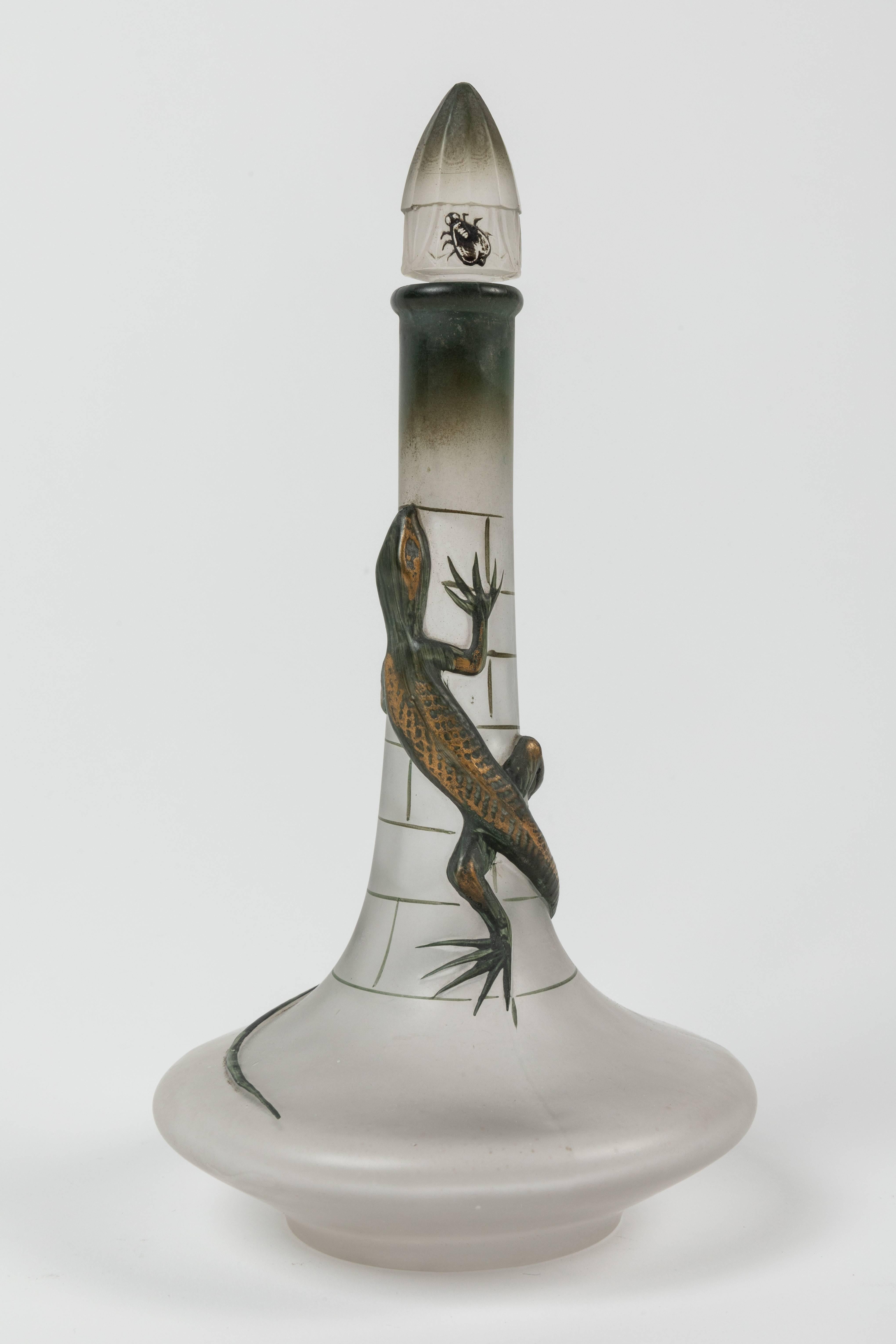 Perfume bottle in frosted clear glass with mounded design of a lizard wrapped around the long stem of the bottle hunting a fly resting on the cap. Designed by Maurice Depinoix in 1912, France. This bottle produced for Lubin's 