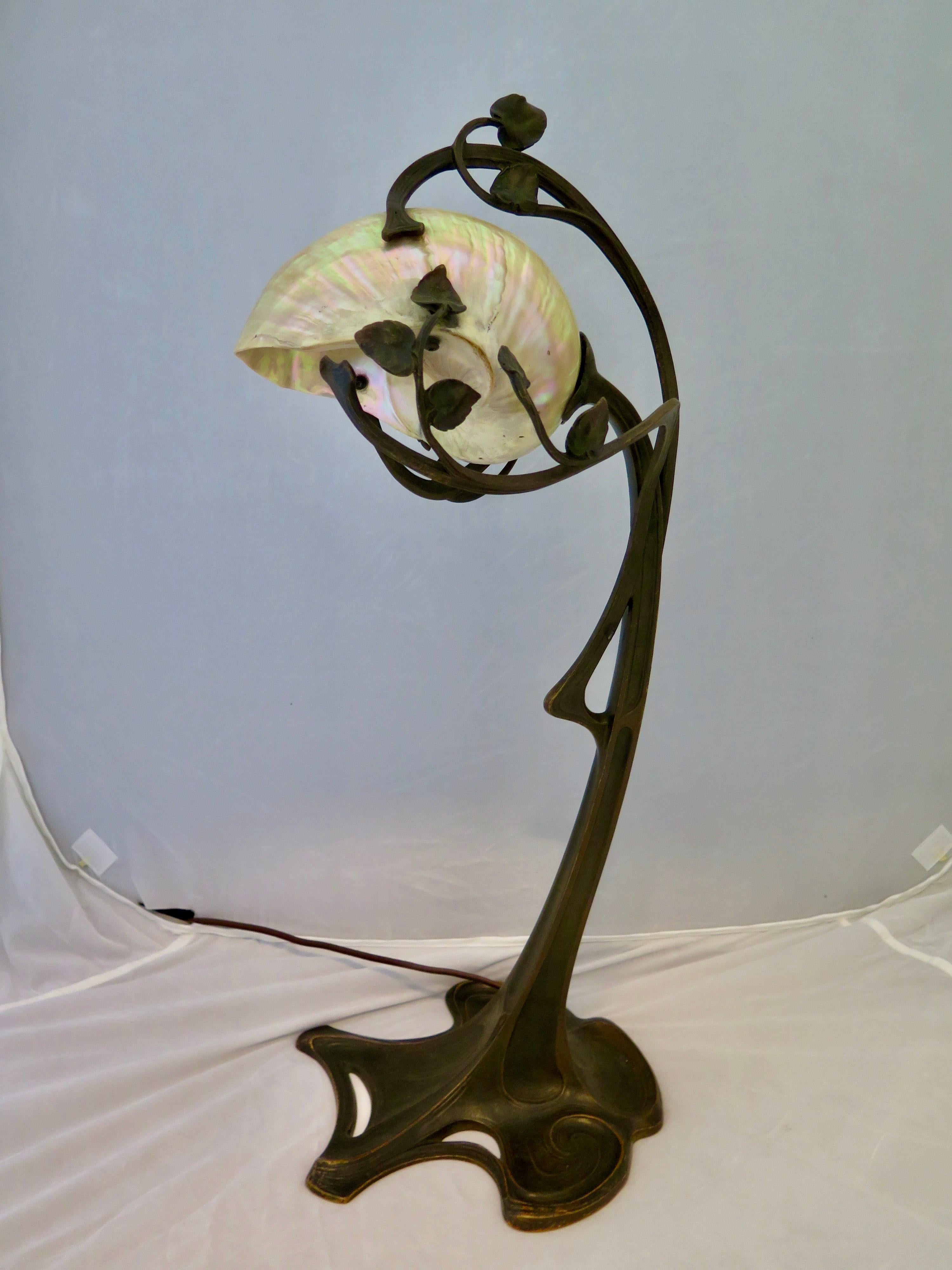 The flowing decorative spiralling vines arching upward and above the stylish patinated bronze base are fundamentals of the French Art Nouveau movement. These vines ultimately embrace a wonderful iridescent conch shell. The conch shell conceals a