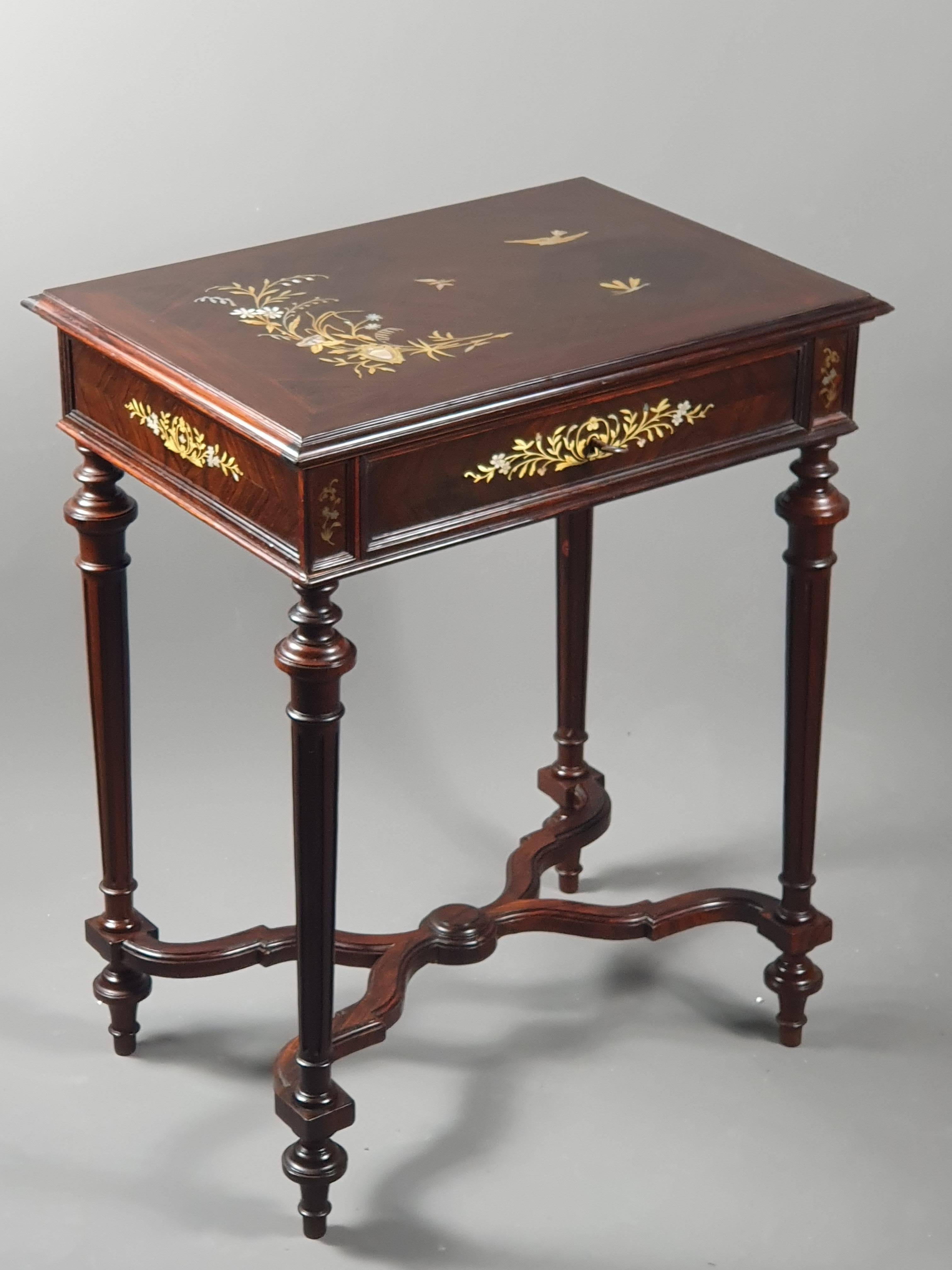 Side table forming a in rosewood veneer and marquetry of brass and mother-of-pearl. Superb top decorated with a floral composition around which a bird, a butterfly and a dragonfly twirl, ornaments in the same spirit on the belt.

Four fluted feet