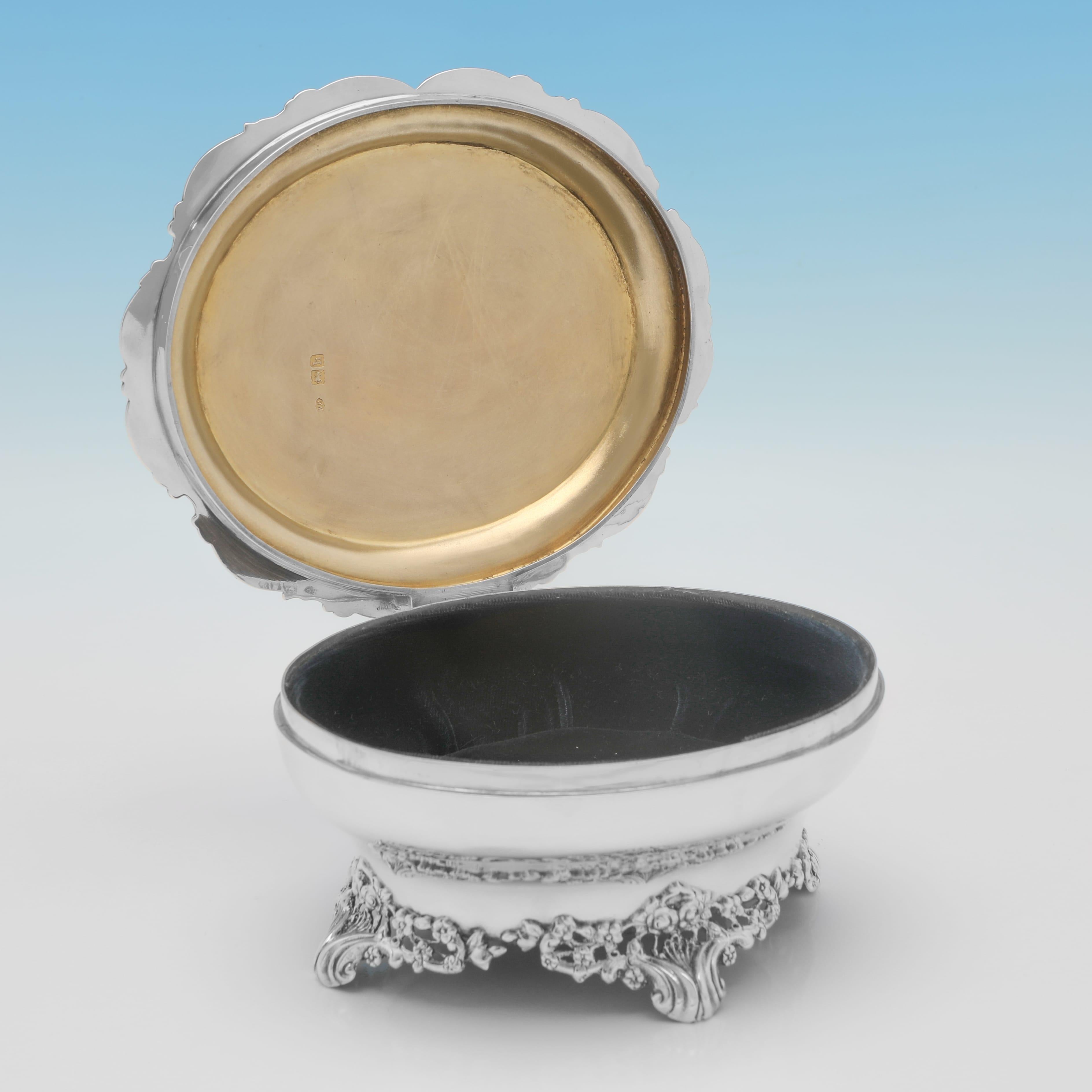 Poinçonnée à Londres en 1903 par William Comyns, cette jolie boîte à bijoux ancienne en argent sterling de l'époque édouardienne est de forme ovale et présente des pieds et des bordures floraux moulés et appliqués, une décoration gravée sur le