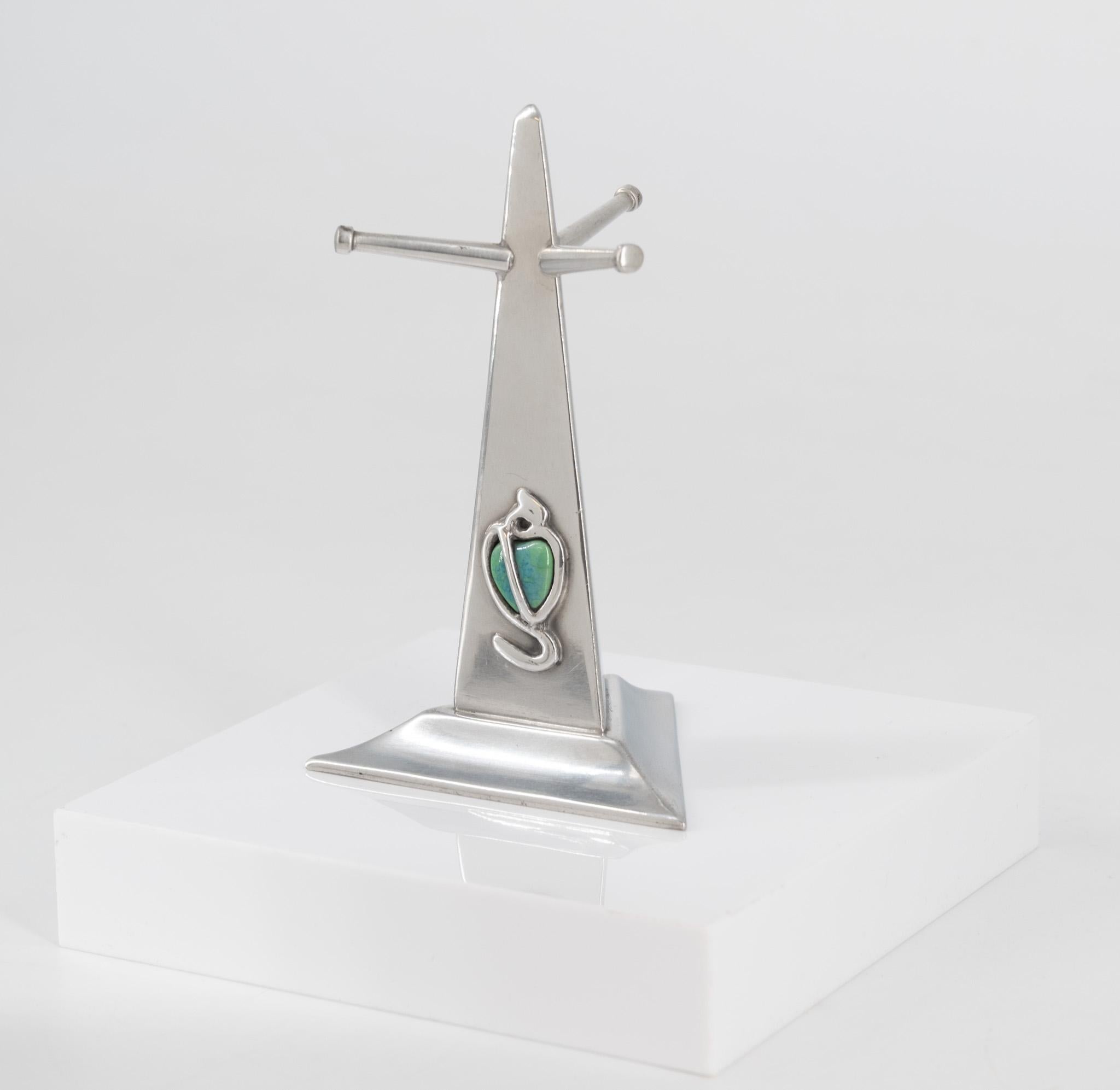 A lovely Art Nouveau pewter & cabochon tree ring stand. William Hutton for G L Connell, London. Circa 1900.

The stand is of triangular obelisk form with applied turquoise cabochon to one side, set between a sinuous knotted tendril design.

In very