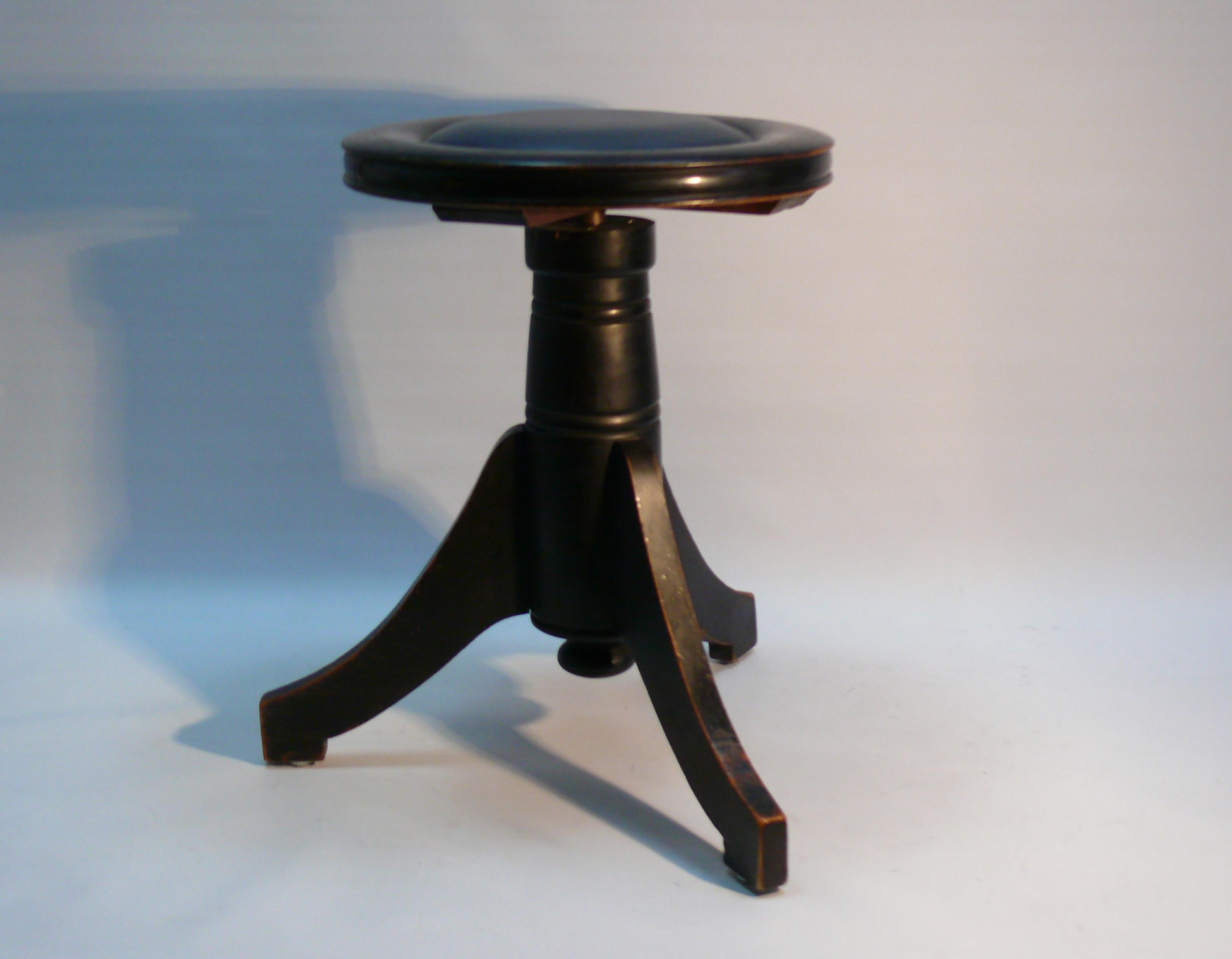 Robusto taburete para piano/taburete giratorio con acabado lacado en negro y asiento acolchado de cuero auténtico. El taburete es de madera maciza y tiene tres patas cónicas. La altura es regulable de unos 50 cm a 65 cm mediante un husillo metálico.
