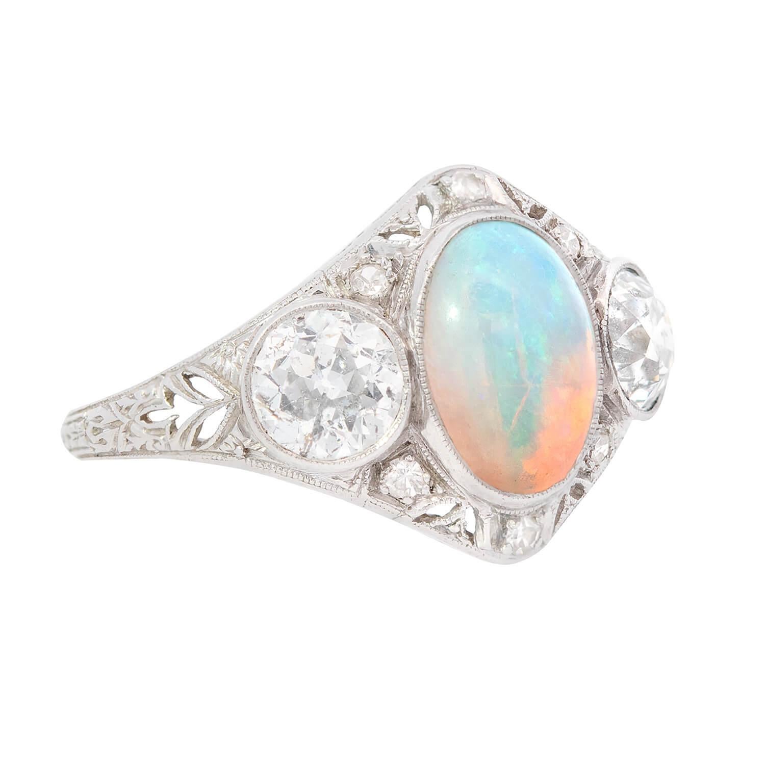 A lovely opal and diamond filigree ring from the Art Nouveau (ca1910) era! Crafted in platinum, the ring holds a central, beautiful crystal opal cabochon, which is held within a bezel setting. The striking opal displays beautiful blue and green