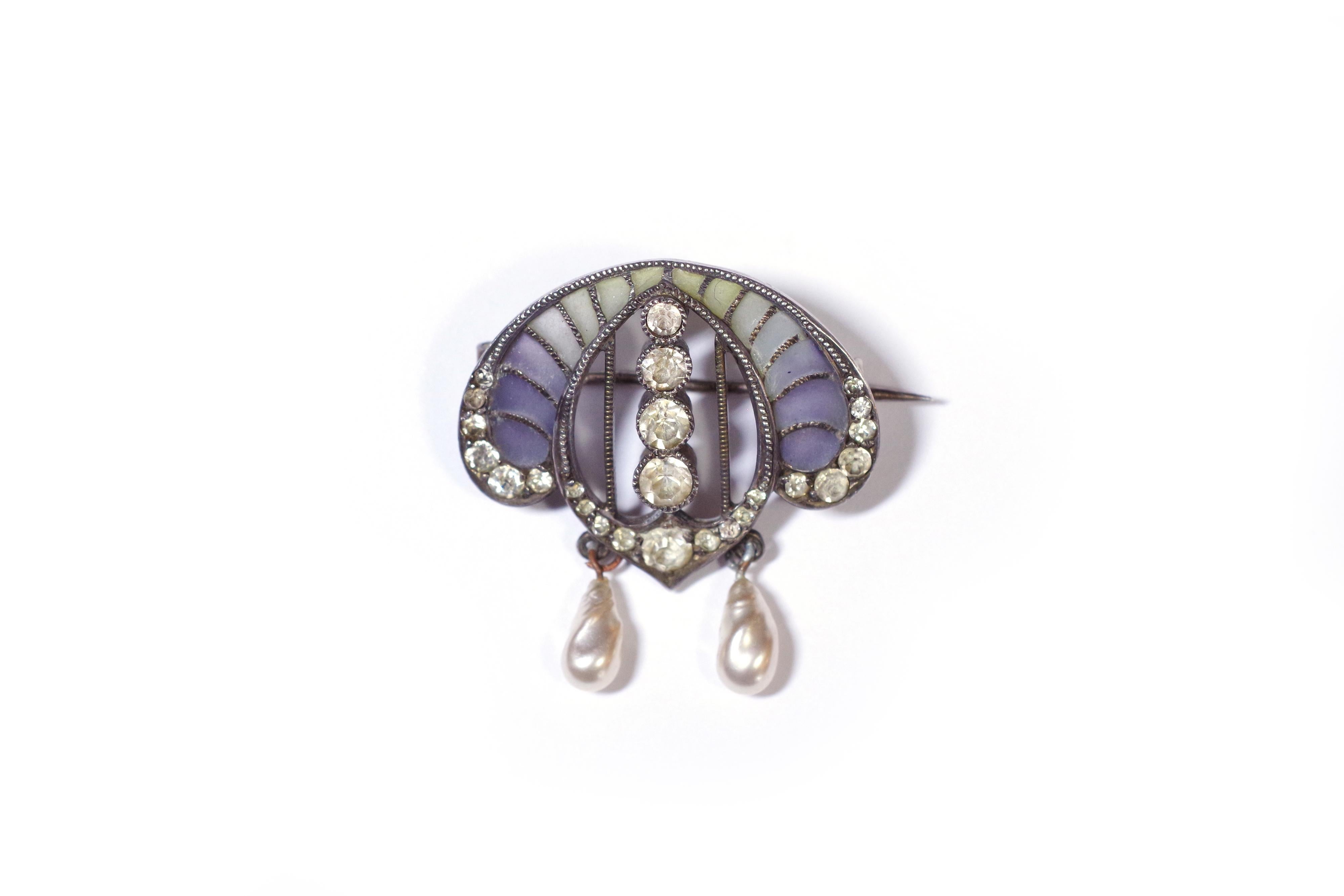Art Nouveau enamel brooch in silver in the form of an arc of circle. The brooch is set with paste stones and decorated with matte plique-à-jour enamel ranging from green to purple. Two imitation pearls are suspended below the brooch. Jugendstil