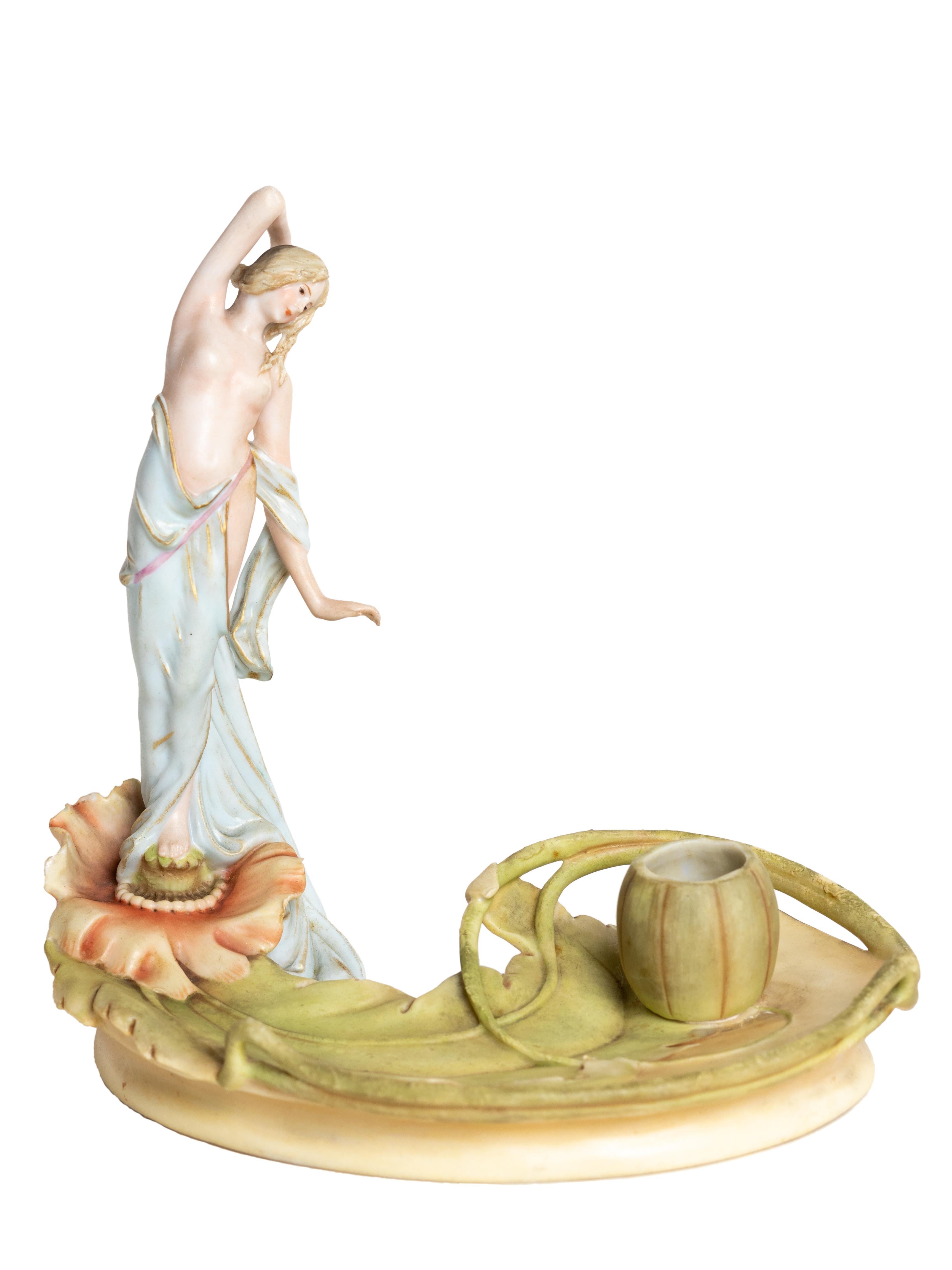 This 19th century porcelain inkwell features a graceful figure of Venus rising from a water lily.

Created by Alois Hampel and marked “3359”, this piece was produced by the renowned Duxer Porzellanmanufaktur in Bohemia. 
It retains the original