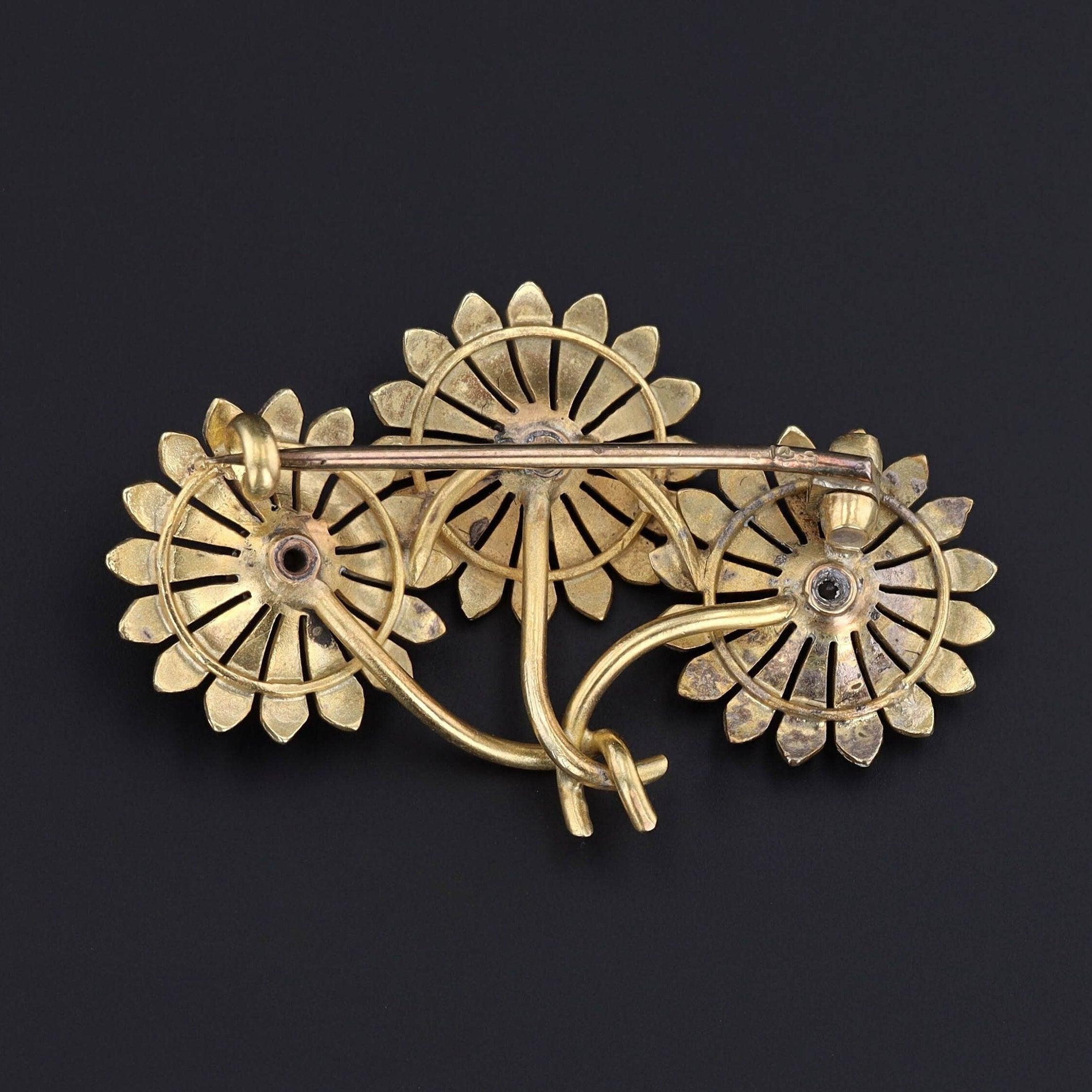 Questa spilla antica (circa 1900-1909) presenta tre fiori di margherita in oro 14k ornati da smalto viola e rosa. Un diamante scintillante adorna il centro di ogni fiore.

La spilla misura 1 pollice per 1,55 pollici di larghezza ed è in ottime