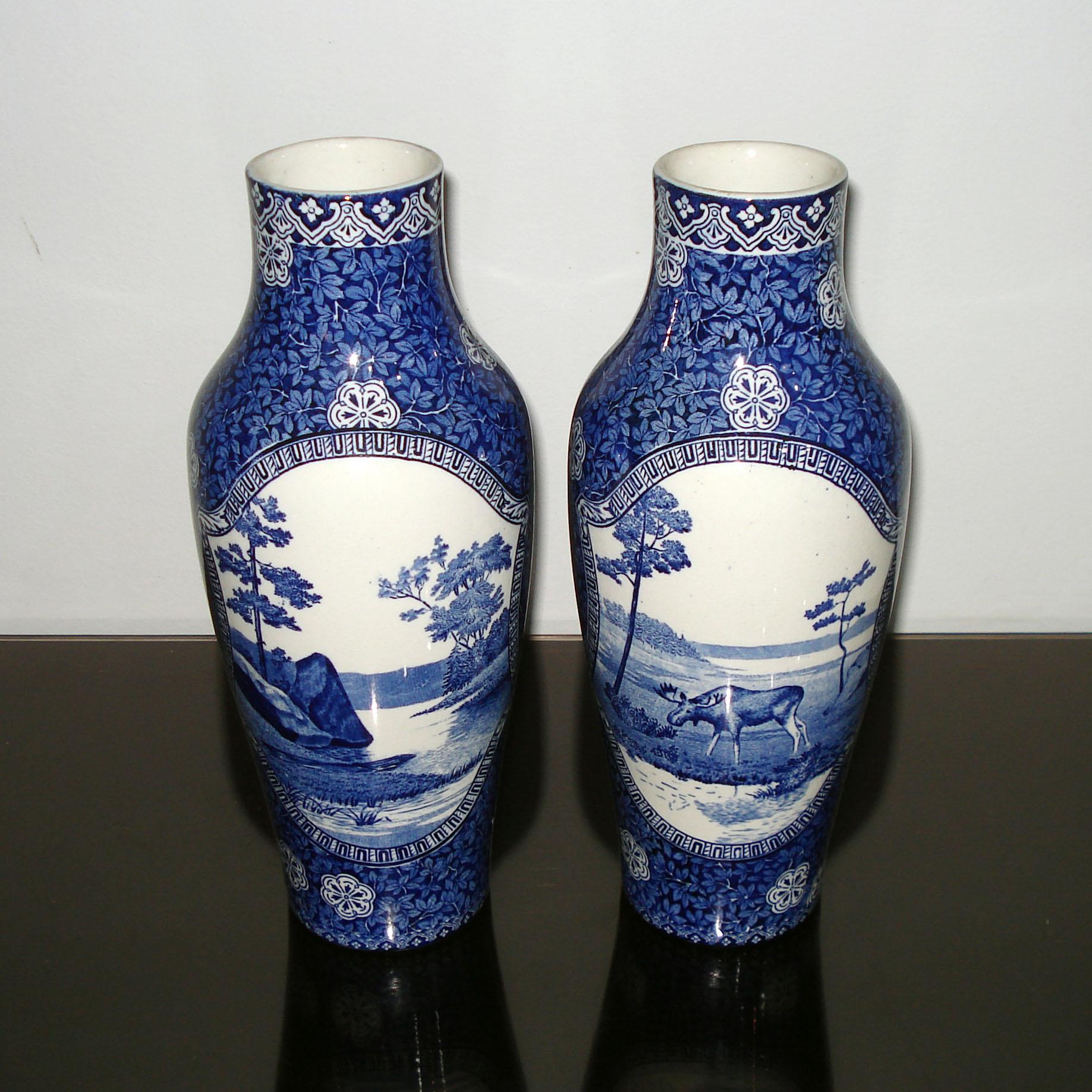 Beautiful and hard to find pair of tall Swedish Rörstrand blue white earthenware vases decorated with alternating medallions of bucolic scenes and floral arrangements on a blue leaf pattern. Each marked on the underside with a blue stamped Rörstrand
