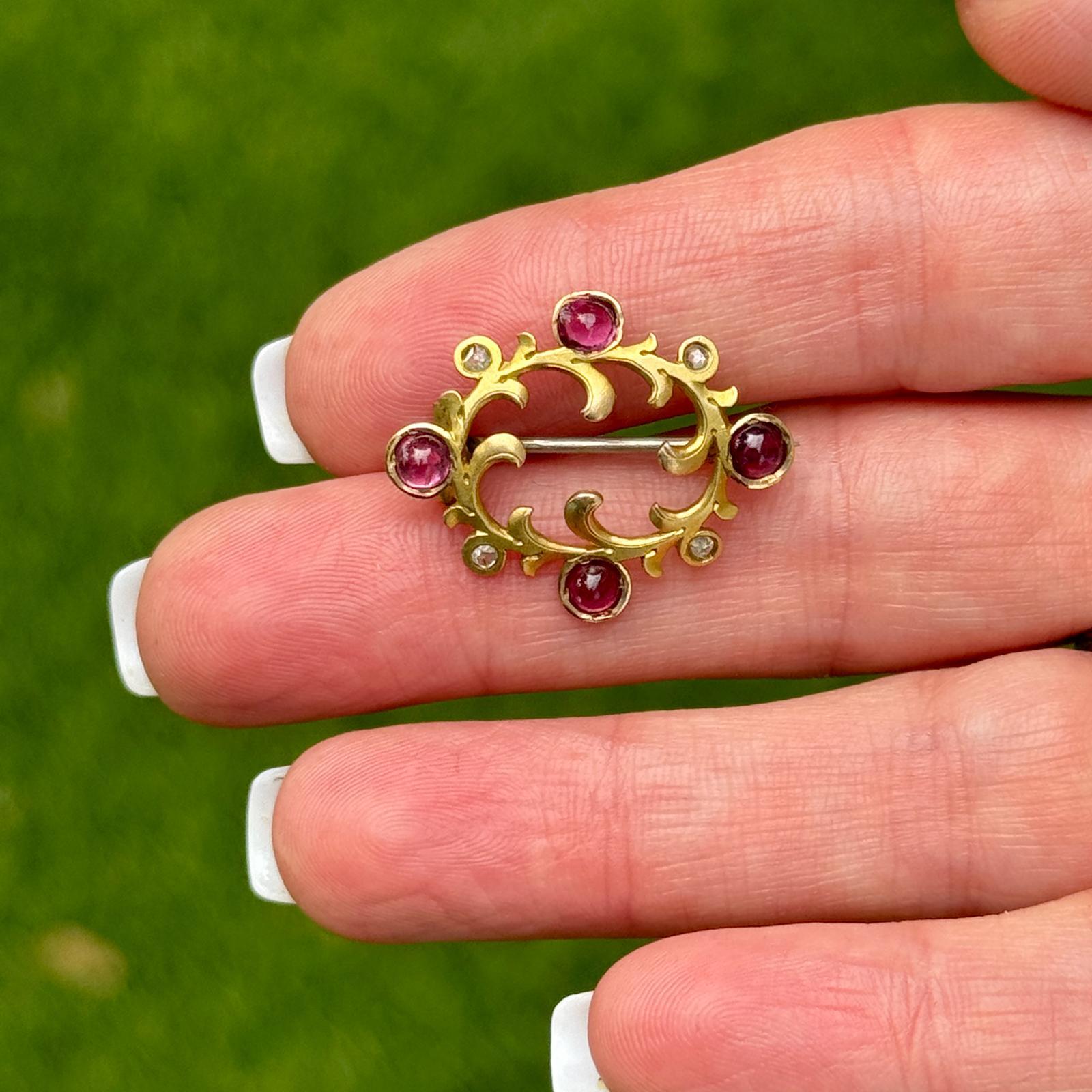 This delicate Art Nouveau brooch is crafted in 14 karat yellow gold and features a graceful design adorned with sparkling rose cut diamonds and vibrant cabochon rubies. The flowing lines and organic motifs characteristic of the Art Nouveau era are