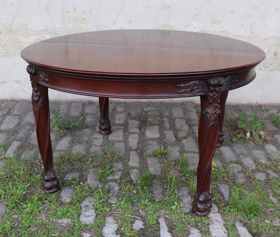 Impressive round dining table with stylized carved legs having flowers and naturalistic foliate decorative motif. The carving, and quality is reminiscent of the French master Louis Majorelle. This example includes the optional center legs and 5