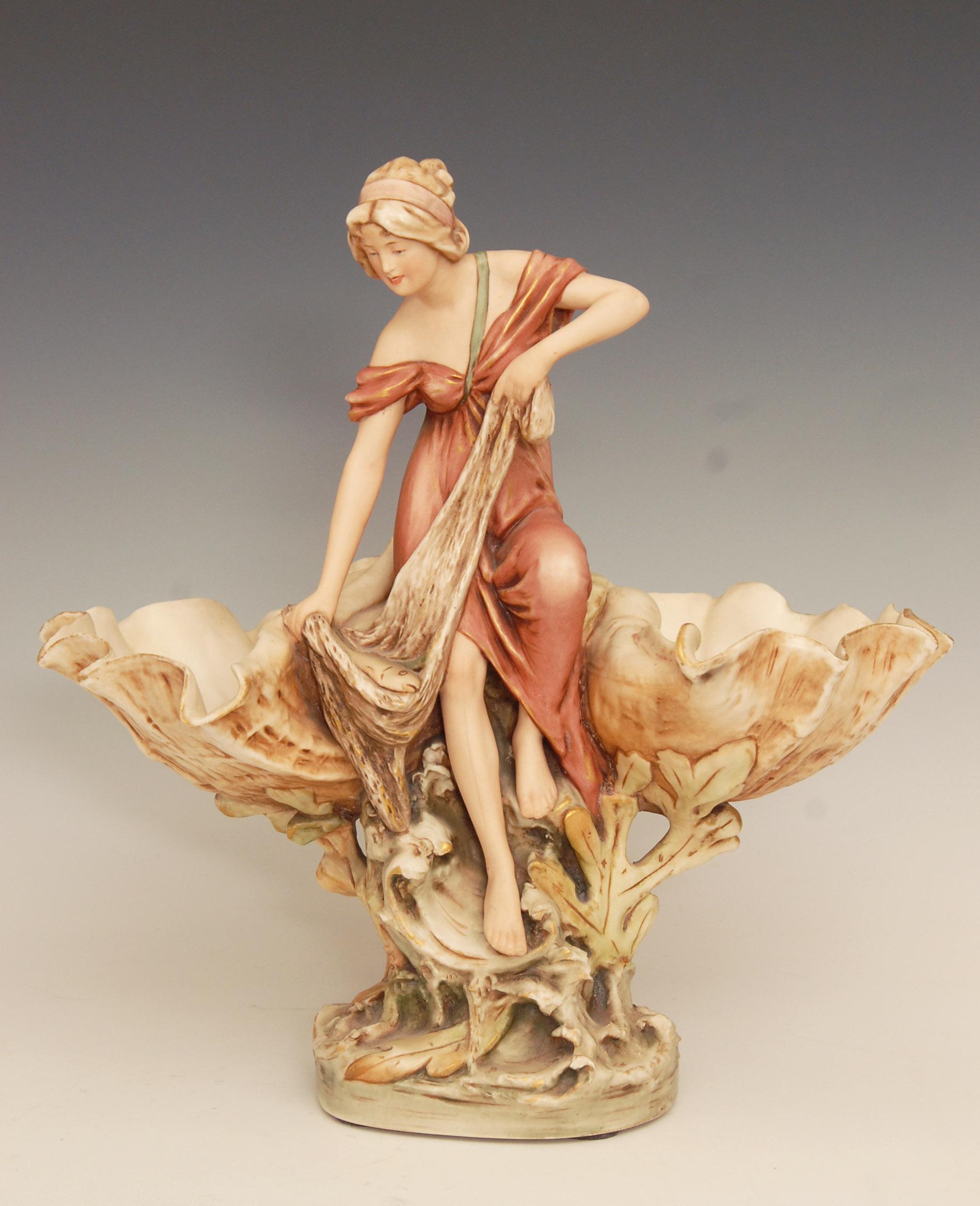 Lovely Art Nouveau Royal Dux porcelain double comport / centerpiece.
Model number 1125 depicting a fisherwoman that has caught a fish in her net, flanked by two giant clam shells. Designed by Alois Hampel, circa 1910.

Measures: 14 inches high.