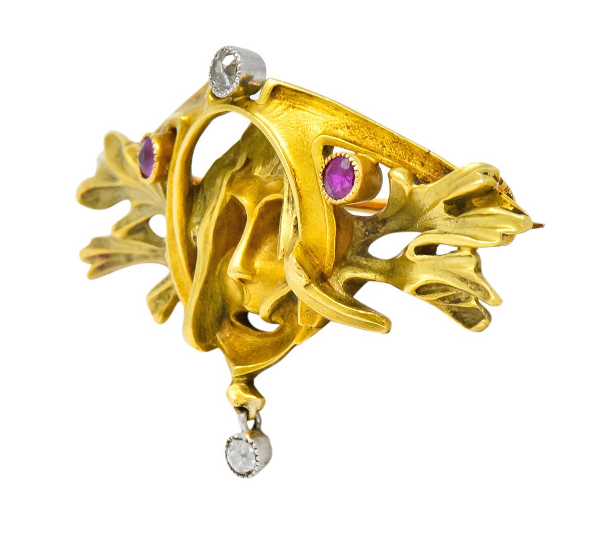 Brooch designed as green man with pierced out features and yellow gold surround

Flanked by detailed green gold foliate and bezel set round rubies weighing approximately 0.17 carat total, semi-transparent and violetish-red in color

With bezel set