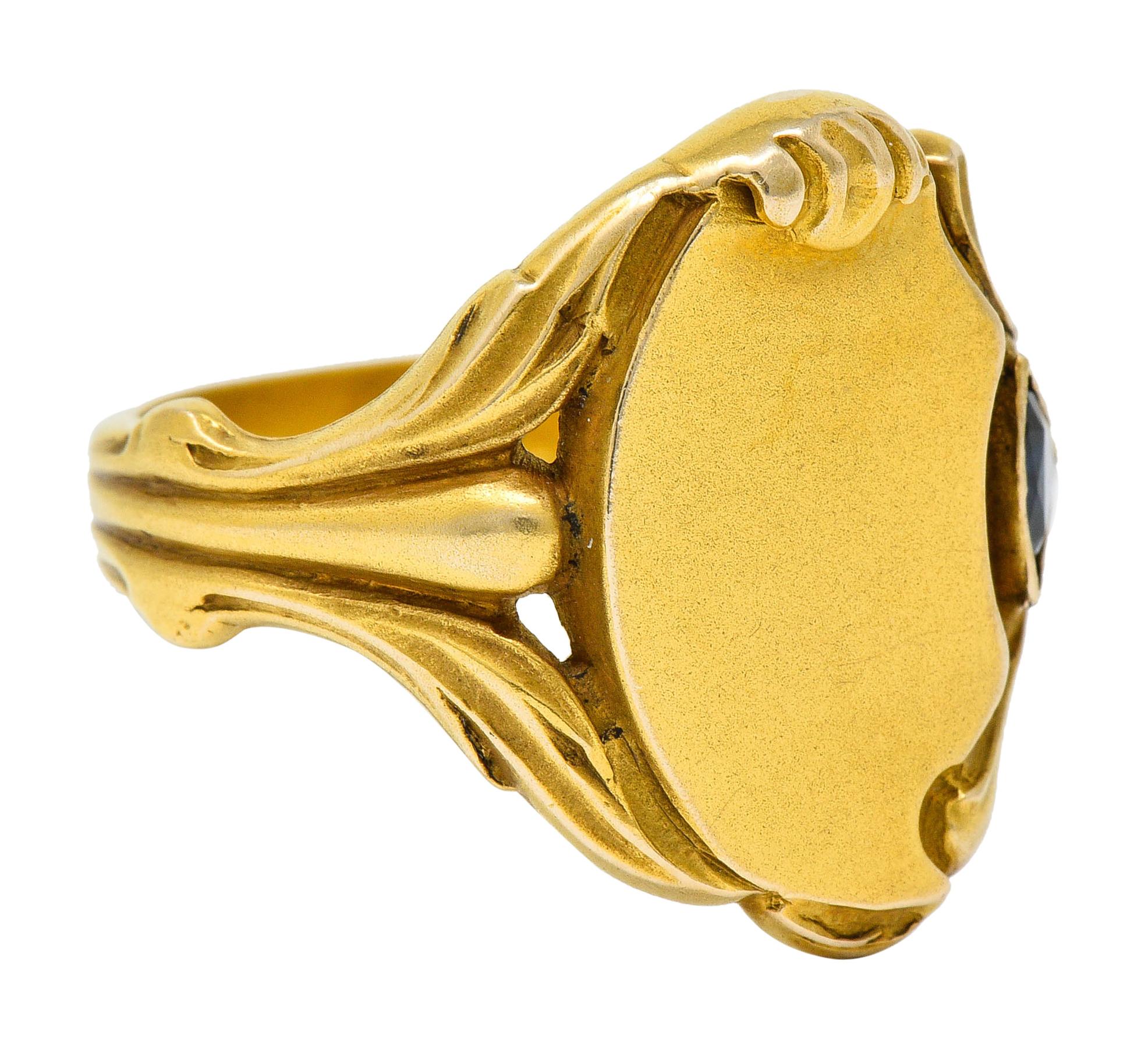 Signet style ring centering a half moon shaped and matte gold surface

Flanked by deeply ridged and whiplashed shoulders, one accented by a trillion cut sapphire

Bezel set with medium-dark royal blue color while weighing approximately 0.25