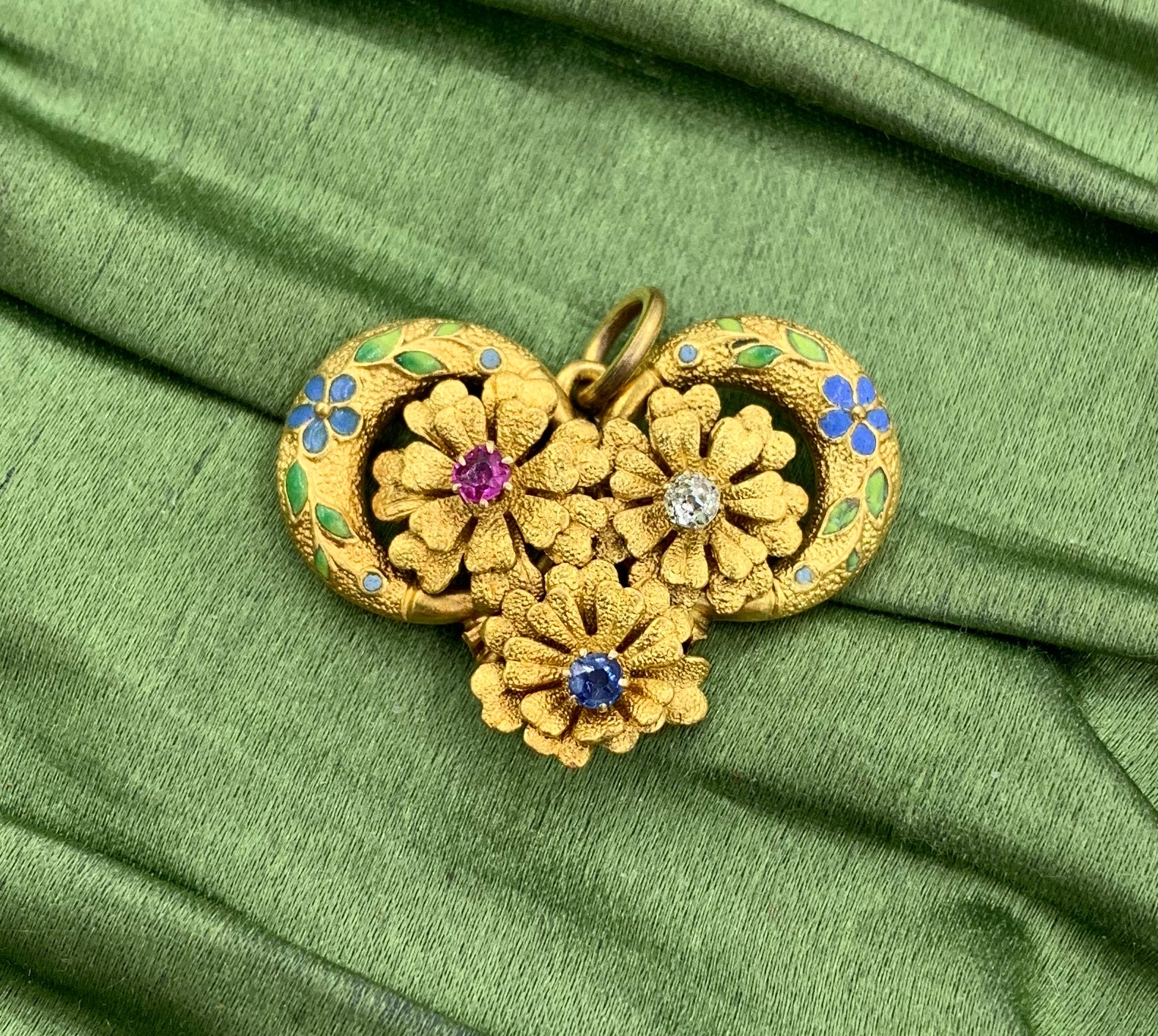 SE TRATA DE UN IMPRESIONANTE COLGANTE ART NOUVEAU ANTIGUO DE ZAFIRO, RUBÍ Y DIAMANTES CON MOTIVO FLORAL EN ORO DE 14 QUILATES CON ADORNO DE ESMALTE DE FLOR DE NOMEOLVIDES.
El exquisito colgante tiene fabulosos diseños tridimensionales de motivos