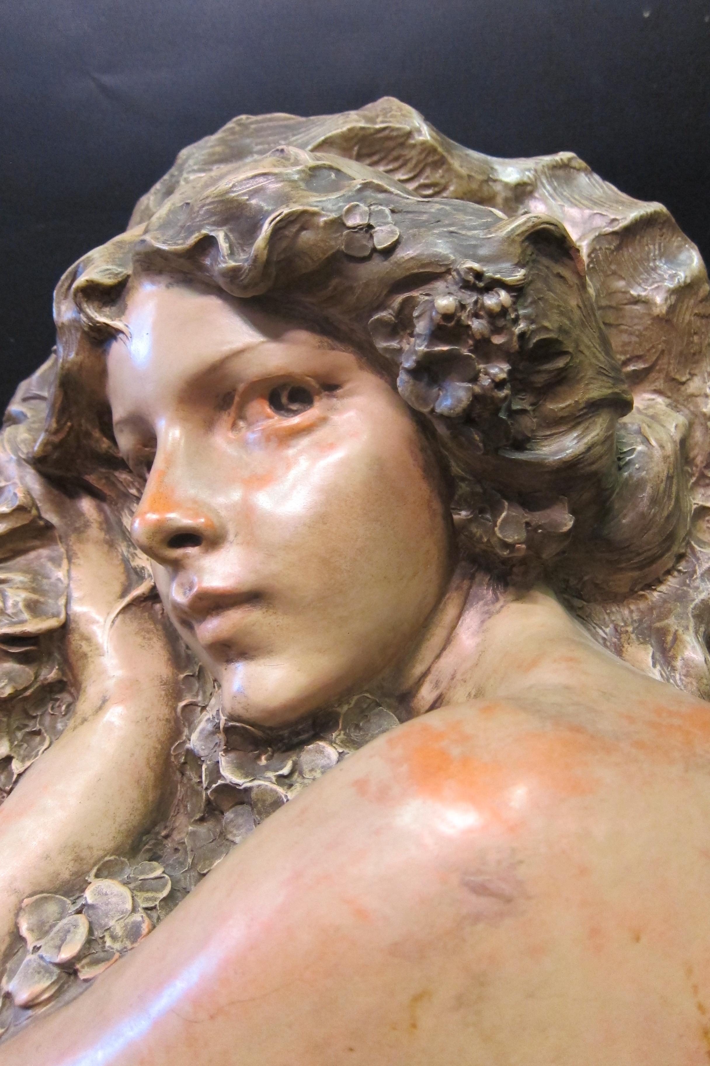 Diese figurale Skulptur im Jugendstil ist in Terrakotta ausgeführt. Es zeigt eine schöne junge Frau mit ausdrucksstarken Augen, die Blumenblüten umarmt. Das Werk ist signiert 