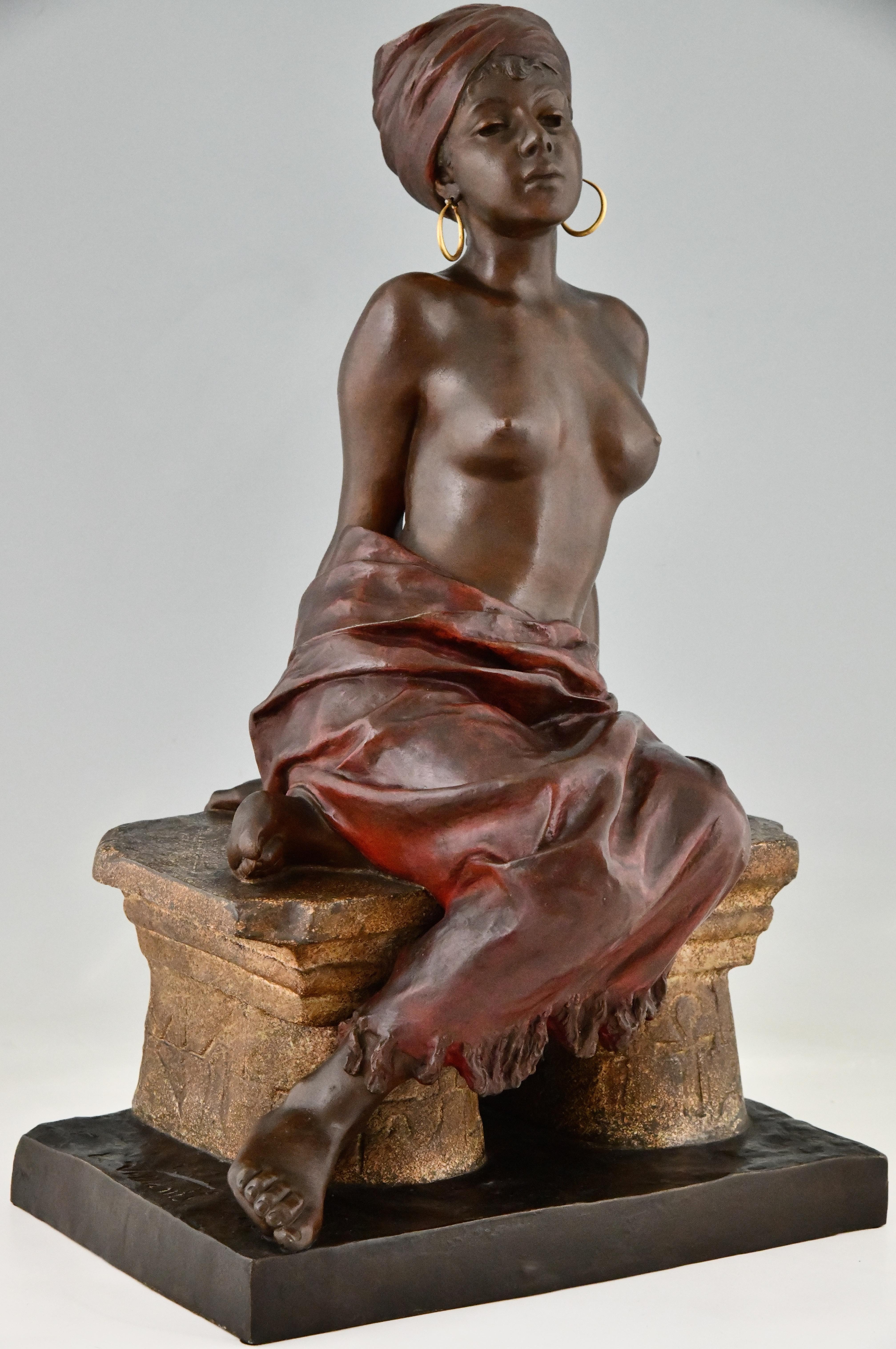 Sculpture Art Nouveau d'Emmanuel Villanis représentant une esclave nue assise. 
Métal d'art, patine peinte à froid. France 1900. 
H. 60 cm. 
Une esclave à demi nue assise sur un banc de pierre, les mains enchaînées dans le dos. 
Elle porte des