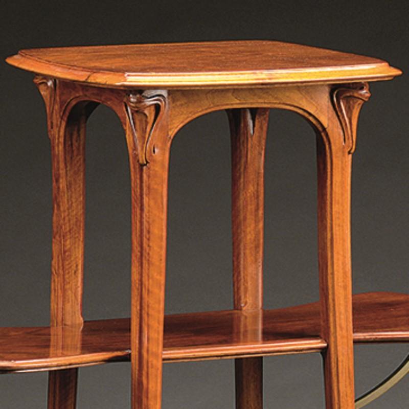A French Art Nouveau walnut wood sellette by Eugène Gaillard. The sellette has three shelves. The middle shelf extends beyond the carved, curving legs in two directions. It is supported by four sinuous bronze arms. There is decorative carving below