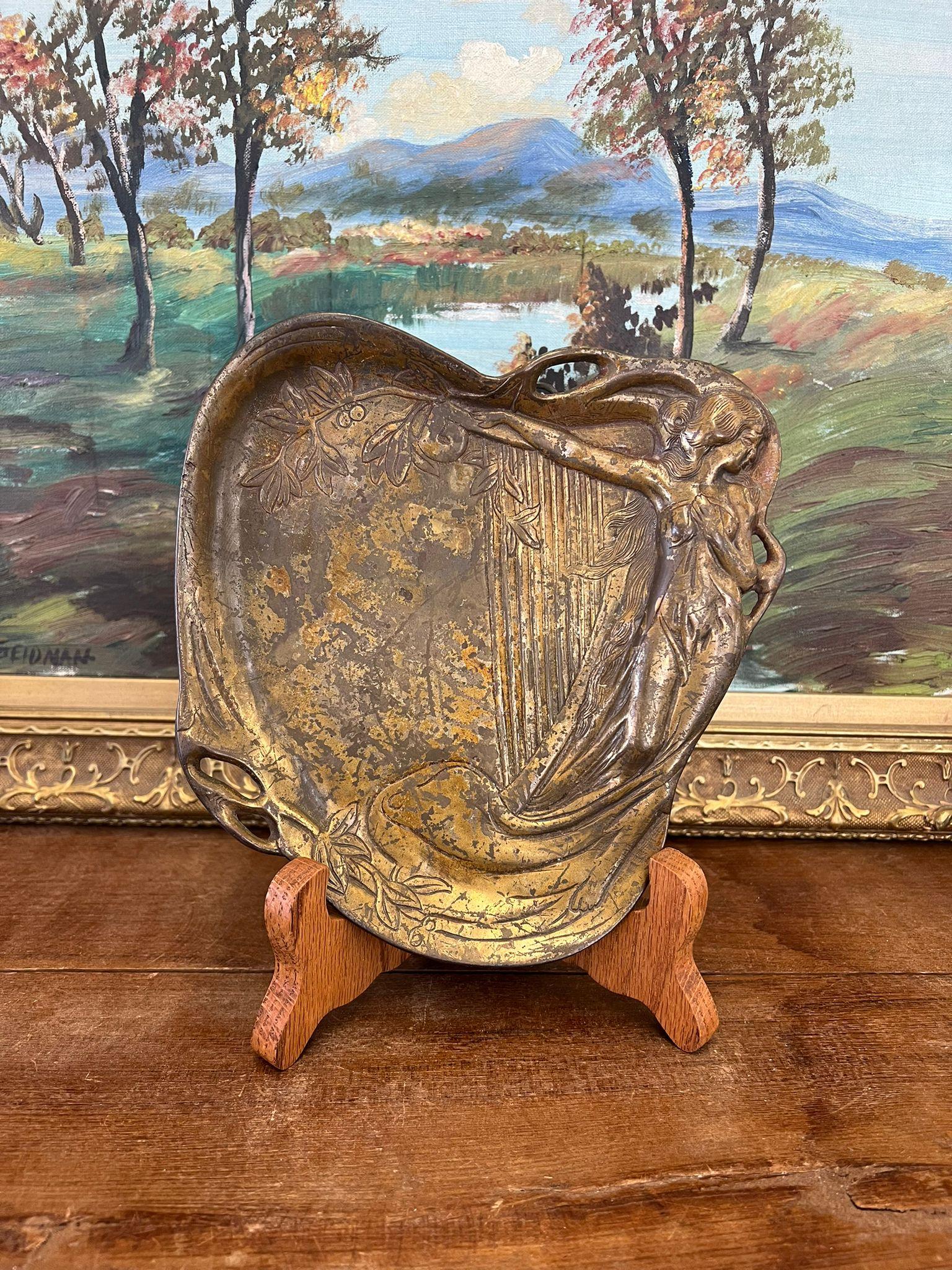 Questo robusto vassoio per bigiotteria o arte da parete raffigura una donna con un'arpa e altri elementi della natura. Questo pezzo ha una bella patina e carattere. Vintage Condit come da foto. L'inserzione si riferisce solo all'articolo descritto.