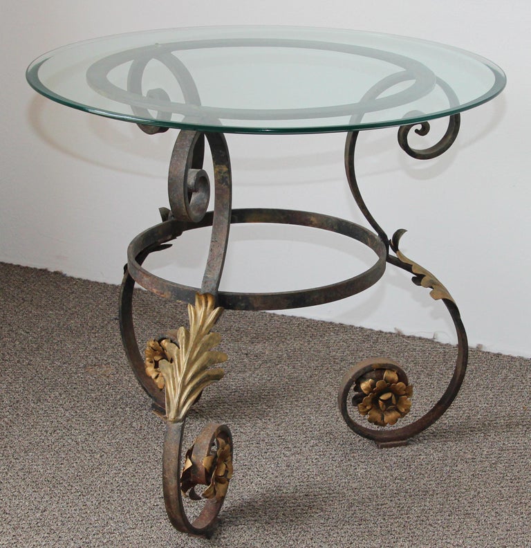 Hand forged Italian Art Nouveau style glass top table with iron frame and gilt metal flowers.
Circa 1930s Italian round glass top table has a curvy iron frame, decorative scroll work accented with gilded leaves, four scrolled legs with gilt metal