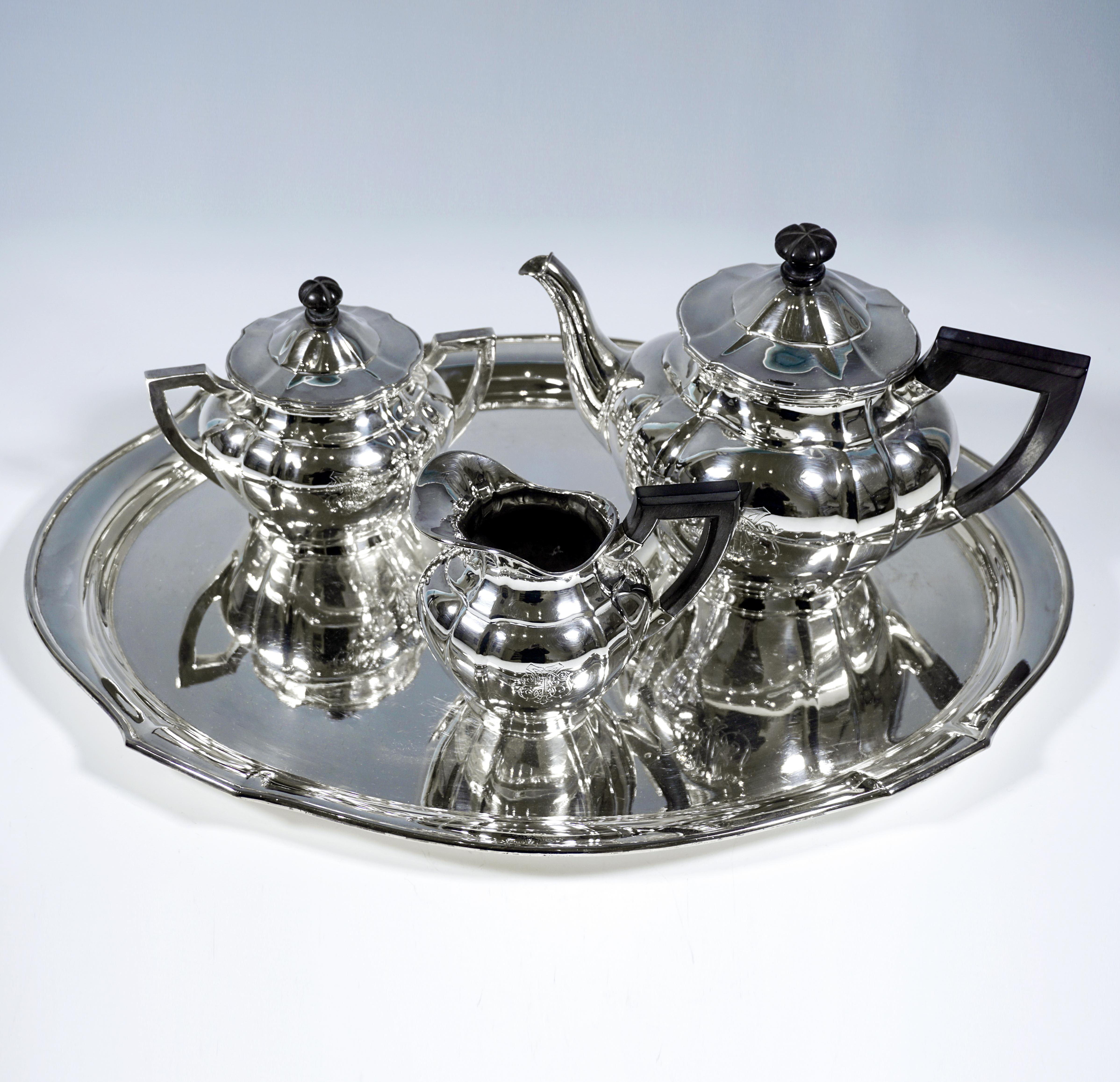 Elegante centro de mesa de plata de 4 piezas compuesto por tetera, lechera, azucarero y bandeja. Forma básica ovalada, pared abombada del cuerpo del recipiente, dividida verticalmente por pliegues en forma de pilastra. Tetera con pico de cisne y