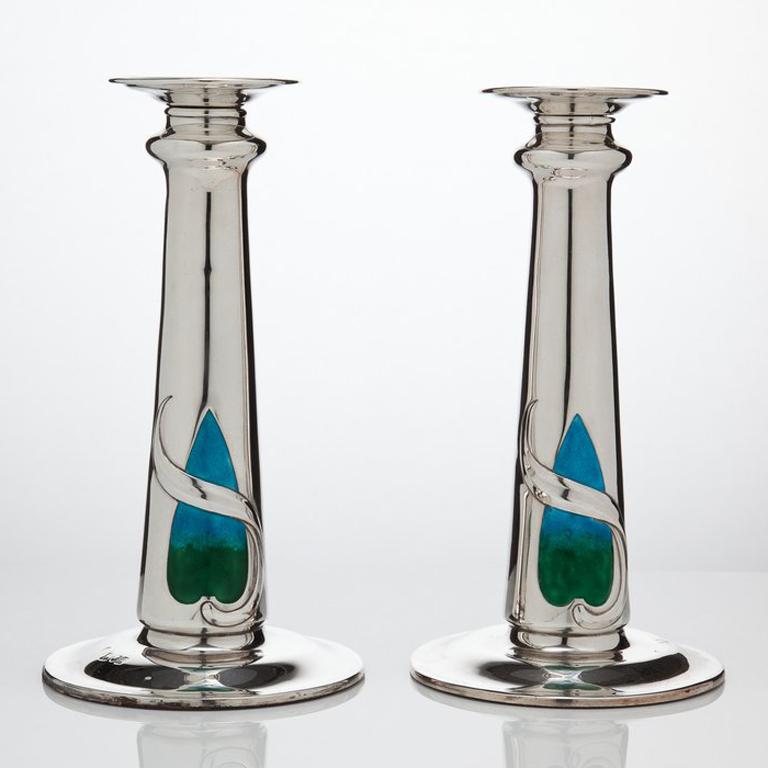 An exceptional pair of Art Nouveau silver and enamel candlesticks by William Hutton dated London 1909.
The enamel decoration is on both sides of each candlestick.
The silver base of the stems is designed to give the visual impression of a pool of