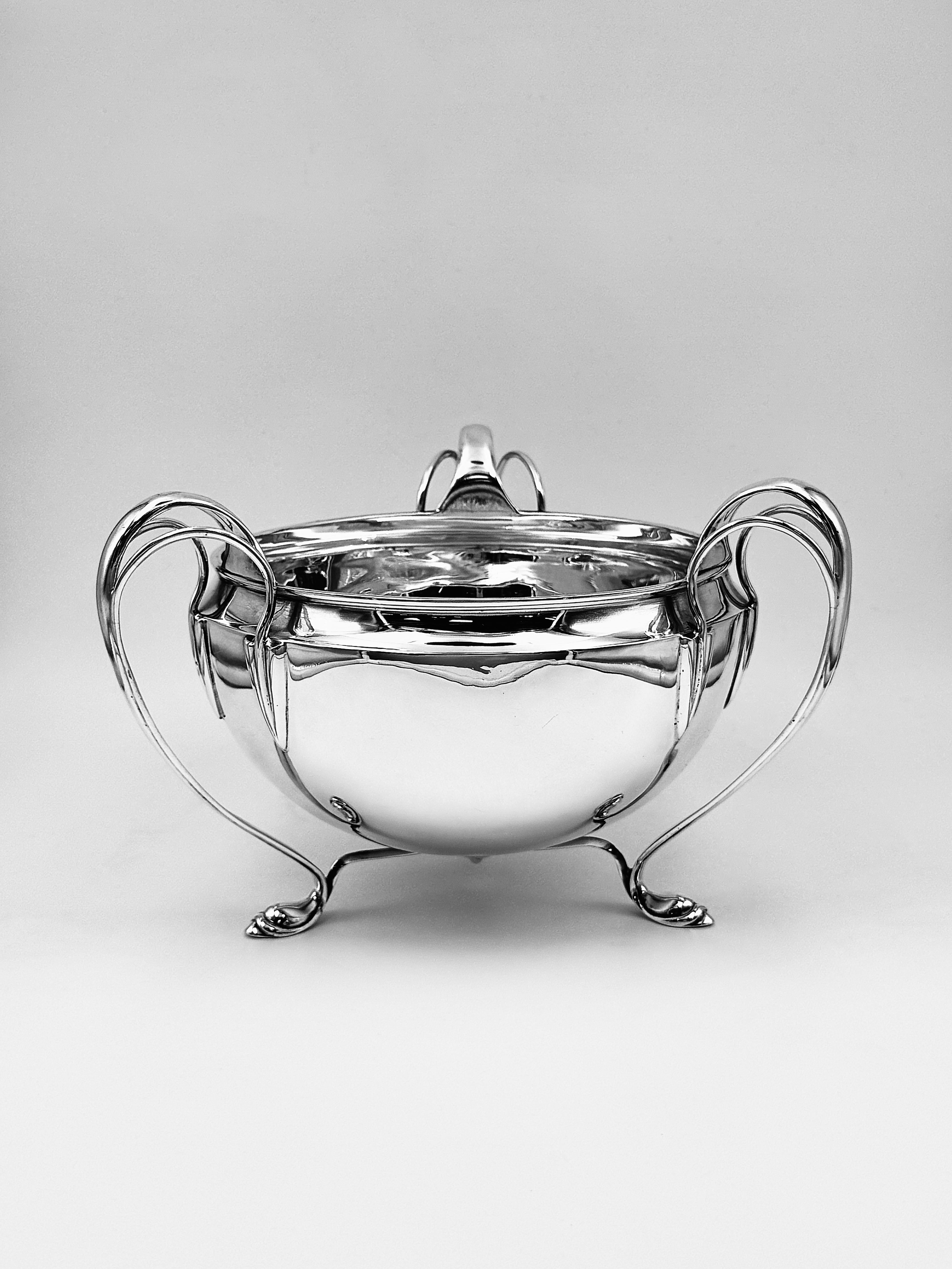 Edwardian sterling silver three-handled bowl by E.S. Barnsley & Co. Ltd, London, 1908. 
Elegant Art Nouveau silver bowl of rounded form raised on three scroll feet which flow out to become openwork handles that curve back to the bowl and join to the