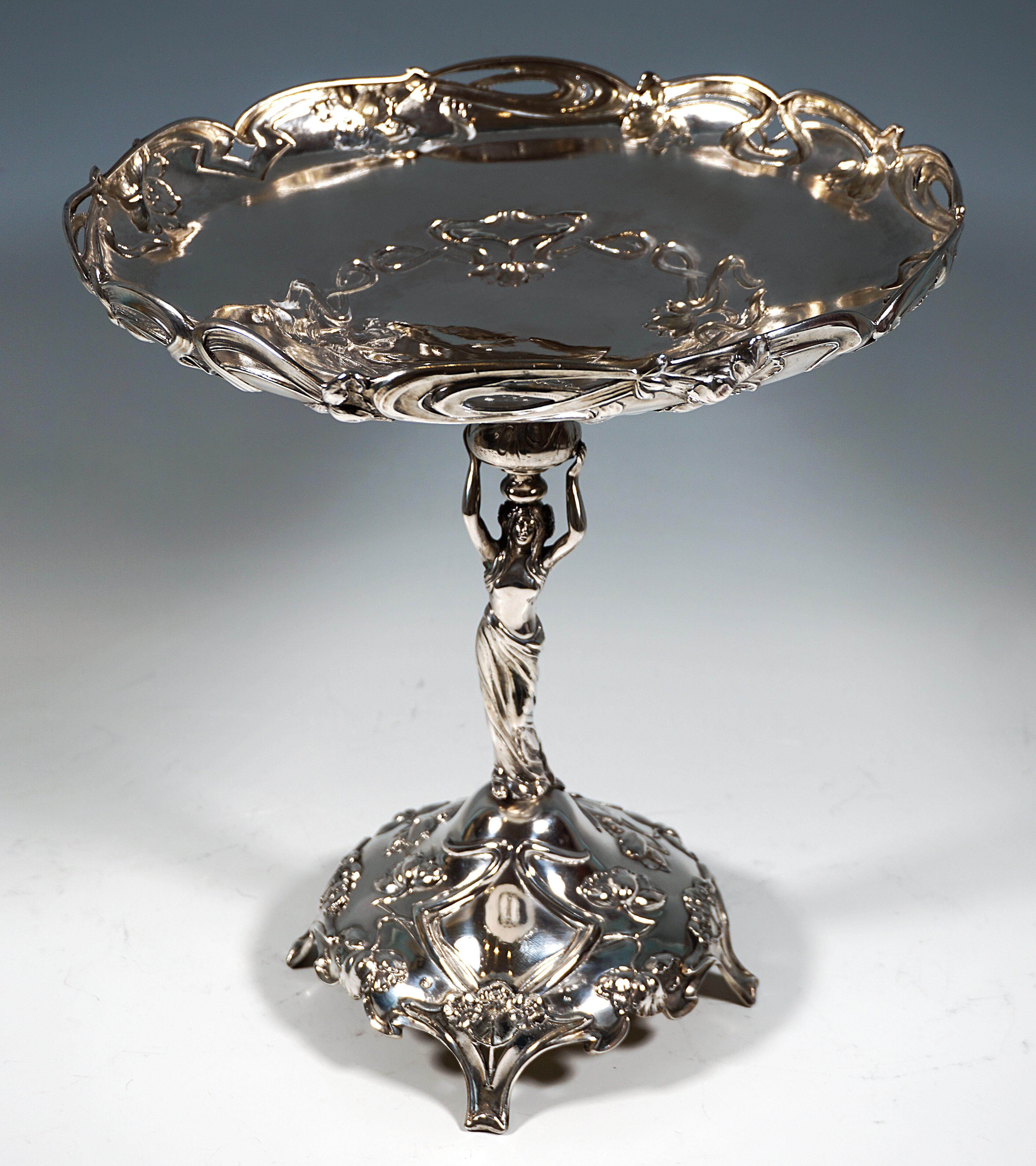 Tall festive silver centrepiece on a curved, funnel-shaped stand on four feet with generous relief decoration of flowers and ribbons as the base for the three-dimensional caryatid in the form of an Art Nouveau beauty, with 
raised arms above her