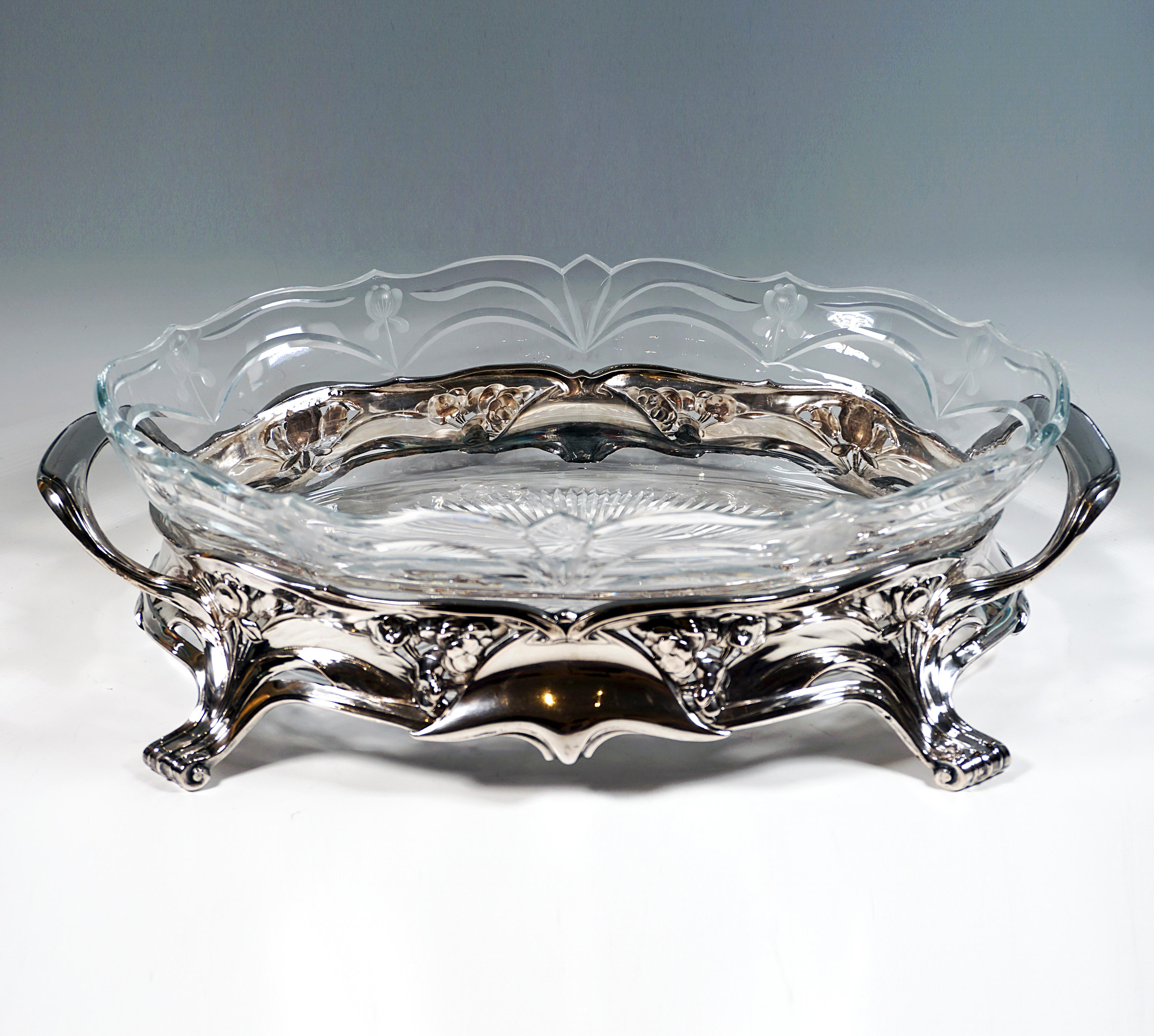 Elegant, festive silver vessel in wide oval base form with four projecting volute feet, on the front and back center asymmetrical panels holding together the surrounding leaf, flower and ribbon braid like clasps, slightly curved top 
edge, on the