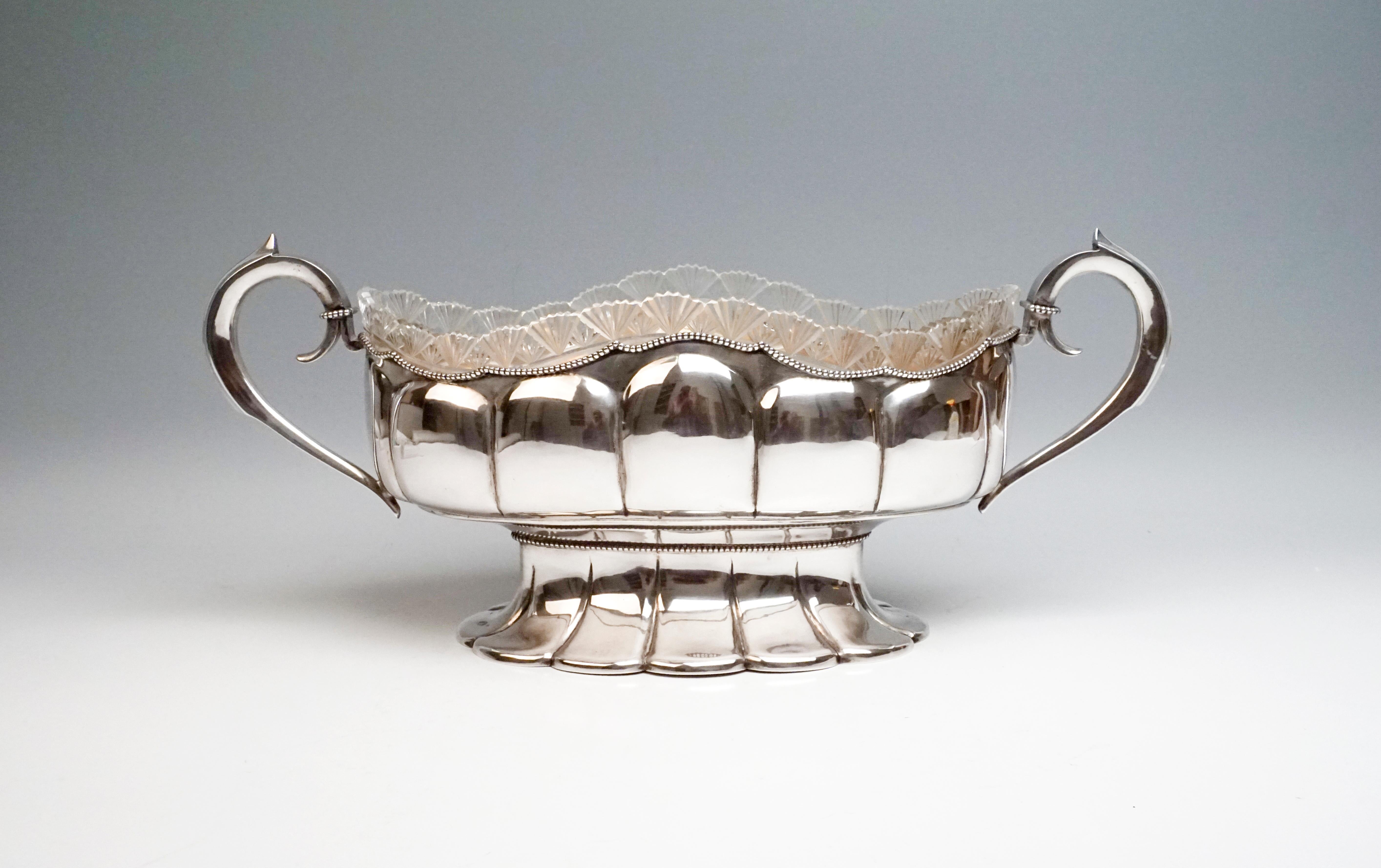 Silver jardinière of oval type
The wall of the vessel is vertically divided by a large-scale hump decor, the folds of which continue in the oval base, set off by a string of pearls, and run out like a fan. The wavy opening at the top is surrounded