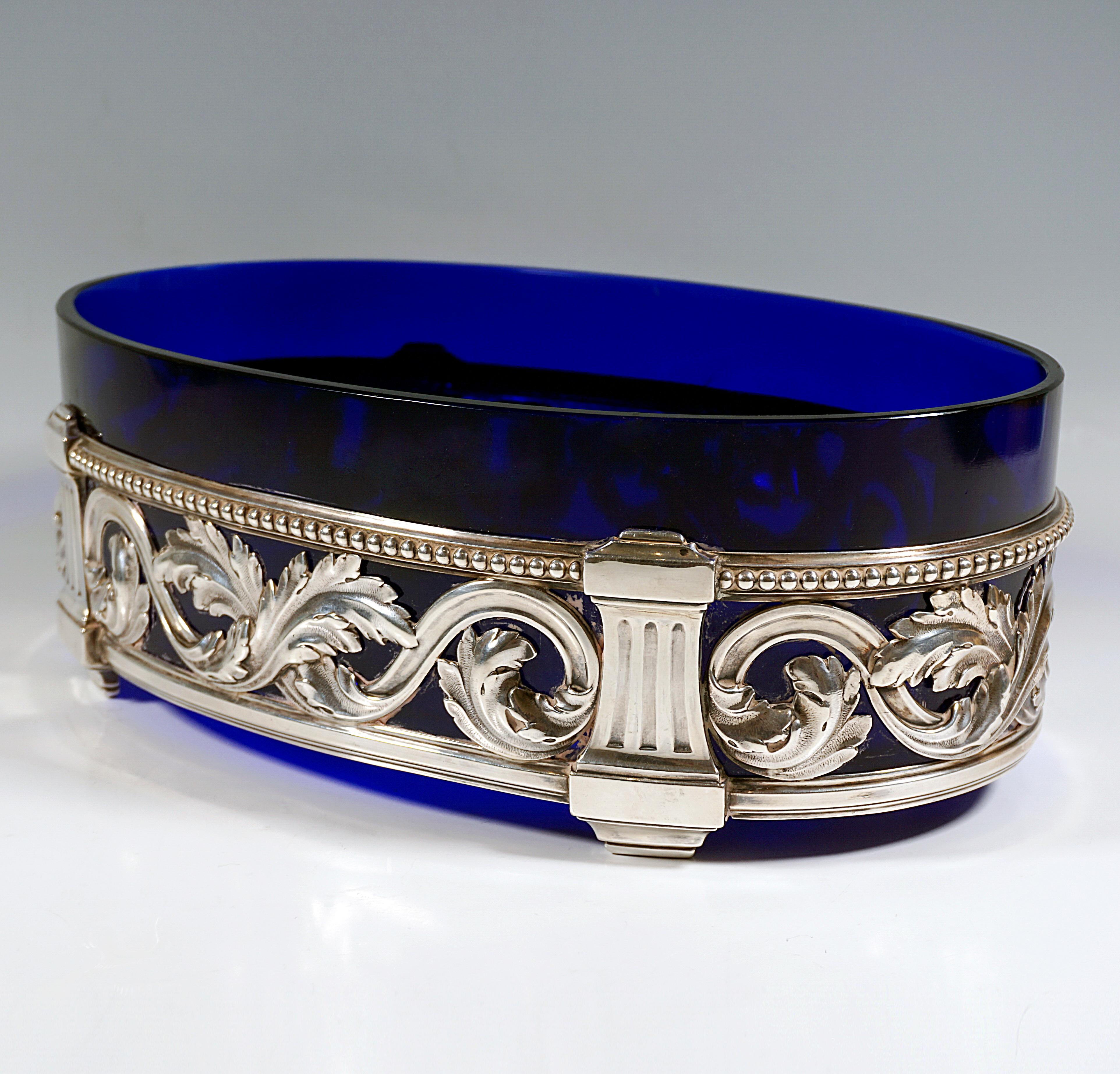 Elegant silver jardinière in the form of an openwork oval band with encircling, intertwined acanthus leaf volutes and beaded decoration on the upper edge, structured by four fluted pilasters with feet, which also form brackets for the cobalt blue