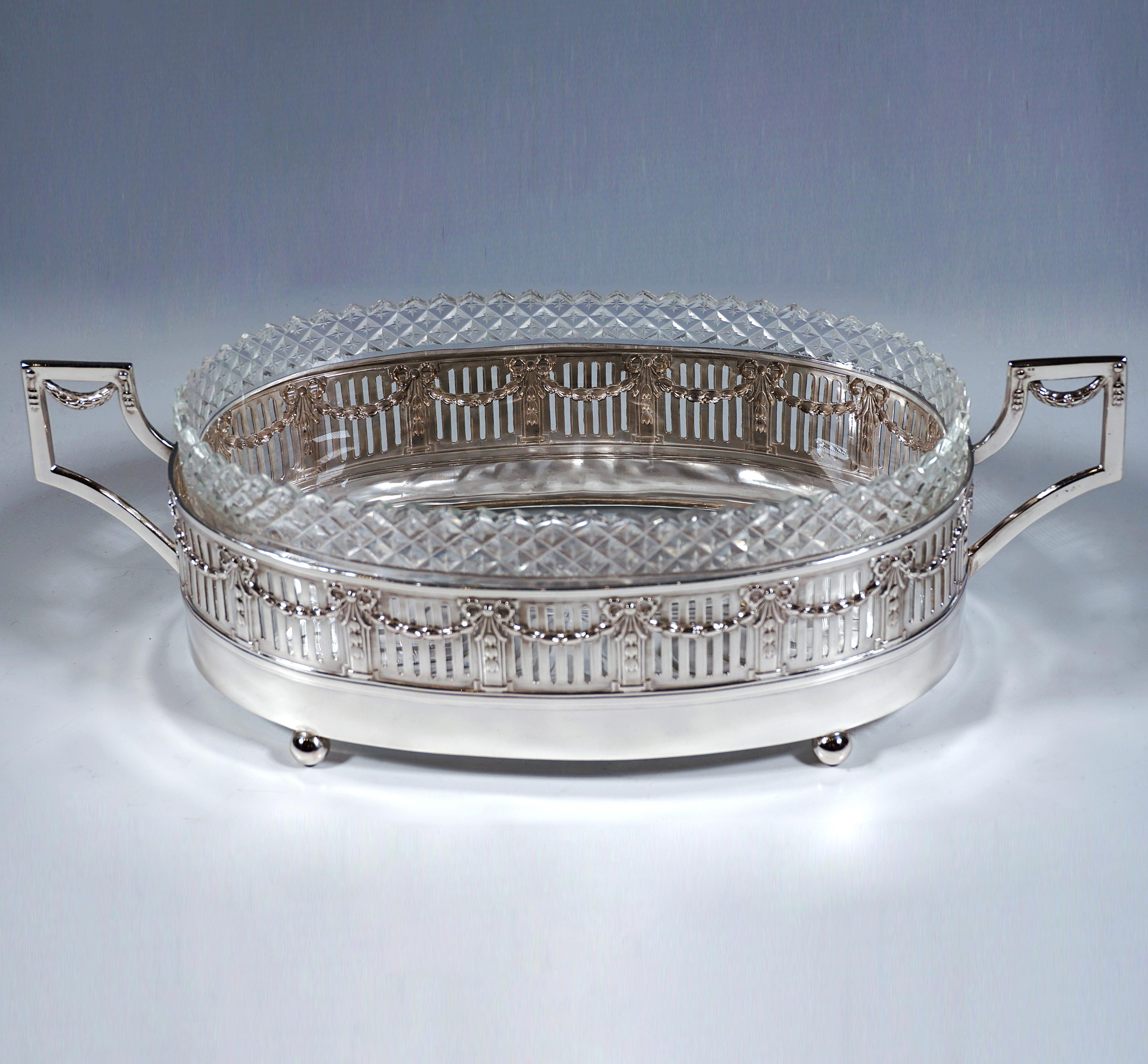 Elegante jardinera de plata en forma de base elíptica sobre cuatro pies de bola, paredes verticales rectas con aberturas verticales regulares, estructuradas por pilastras colocadas rítmicamente con cintas en relieve y festones conectores y