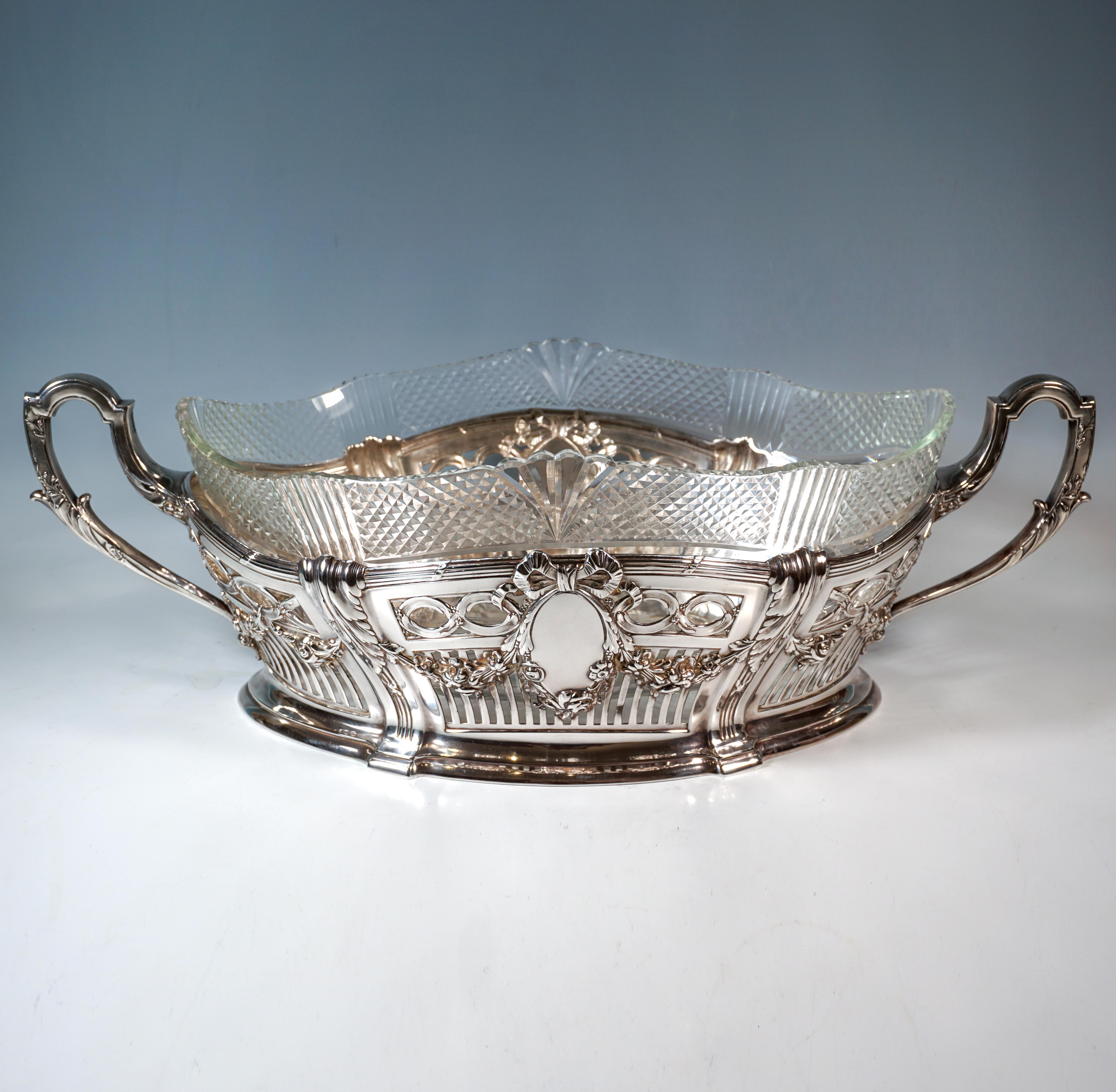 Elegante jardinière d'argento di forma ellittica, con bordo inferiore a gradini, parete curva verso l'esterno e divisa in spicchi da lesene, aperture verticali regolari nella metà inferiore, al di sopra di quella ovale. 
elementi a voluta